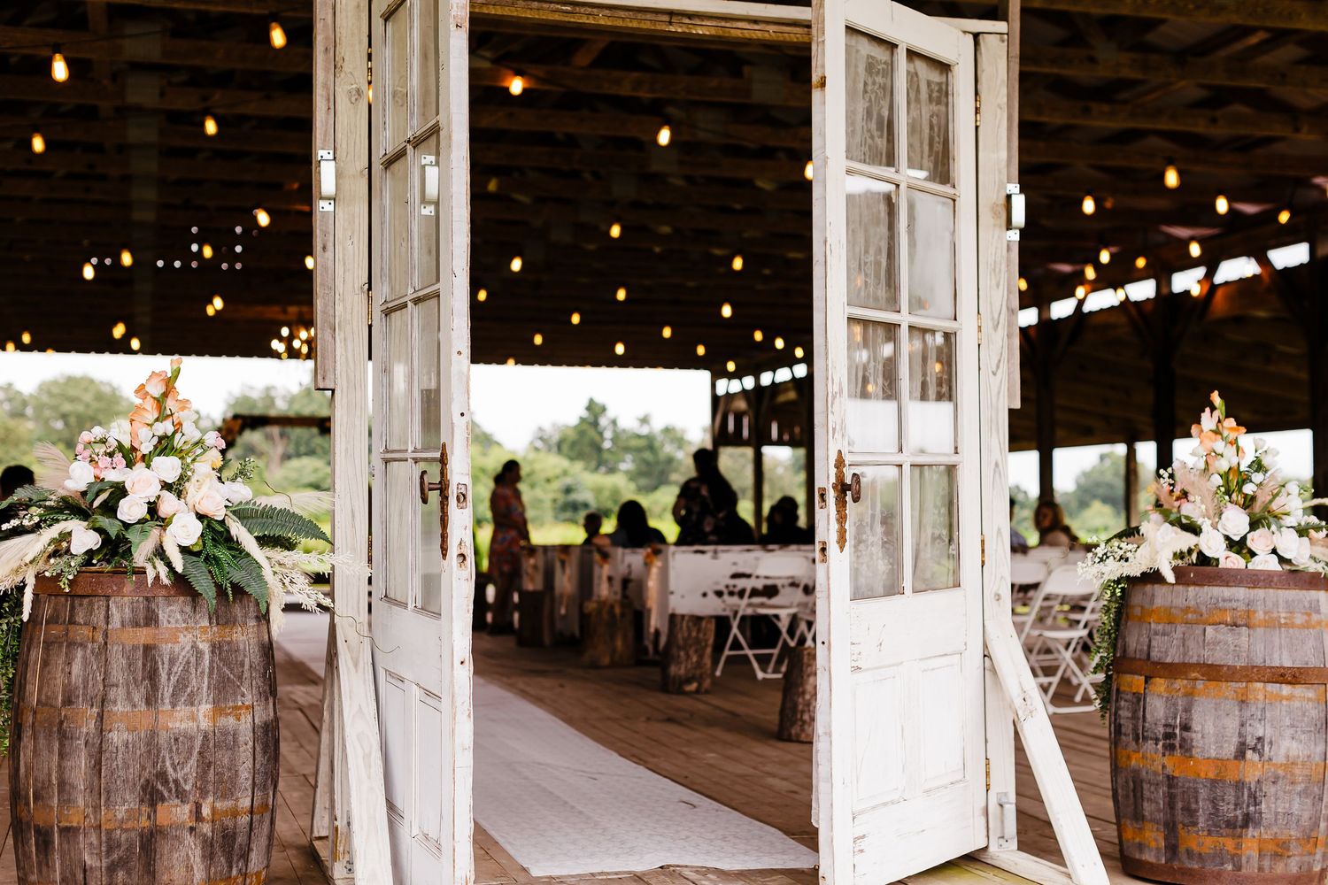 Barn wedding venue interior with string lights and wooden barrel decor.