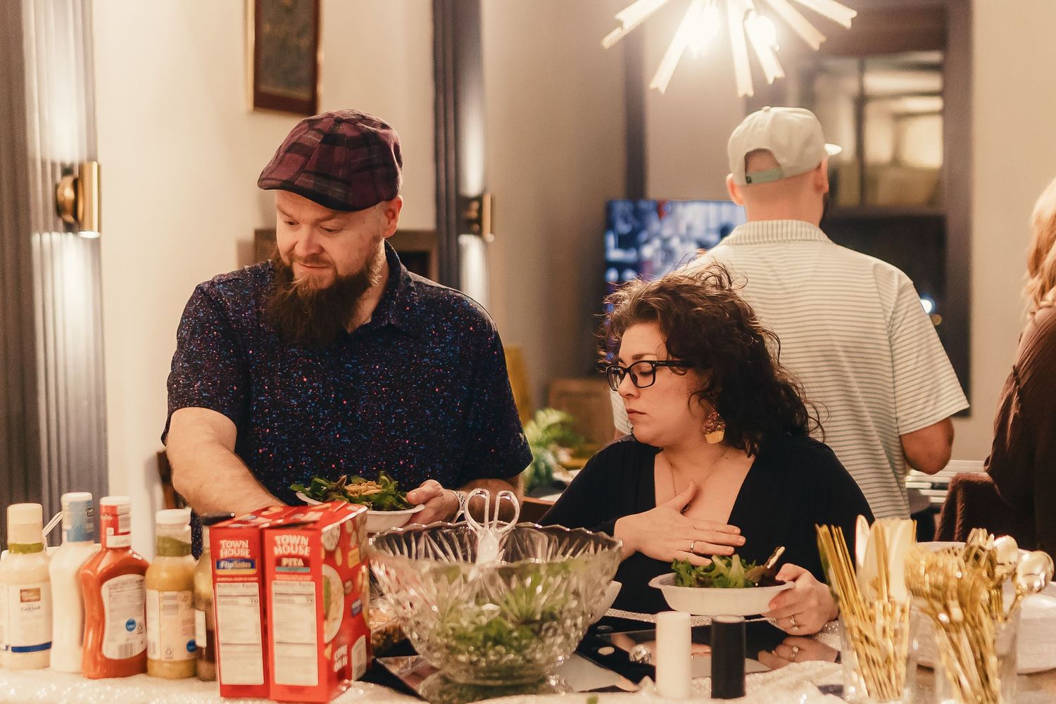 A group of people gathered around a dining table enjoying a meal and conversation in a warmly lit room.
