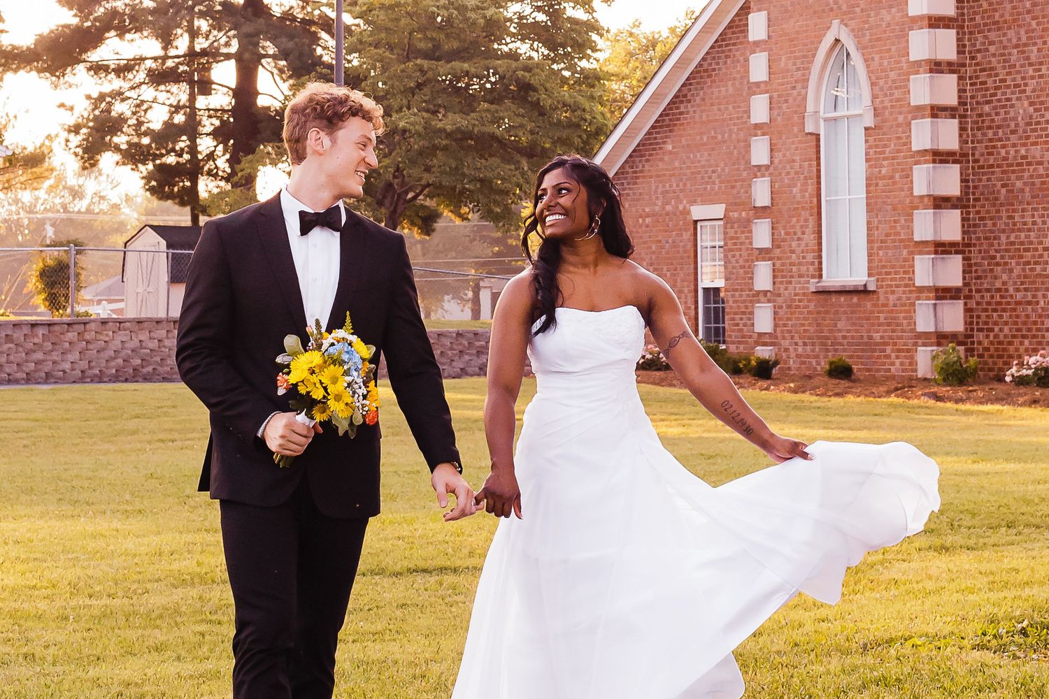 Wedding party poses in front of a brick church during golden hour sunset.