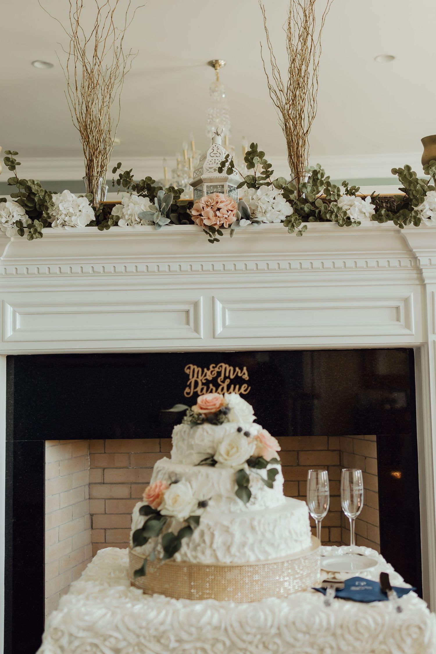 White wedding cake display with floral decorations on a mantle with branches.