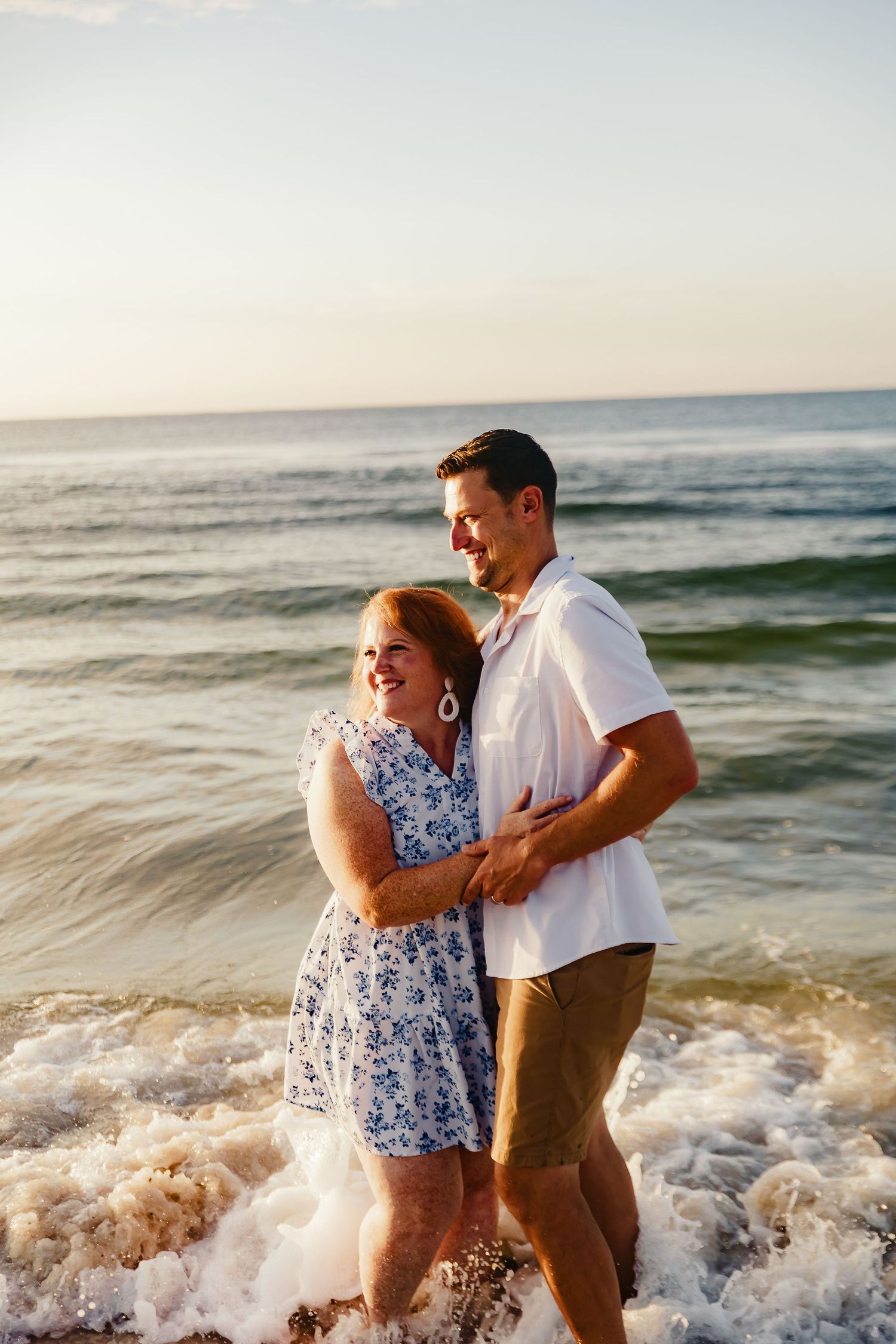 Playful couple splashes in ocean waves during sunset beach photoshoot.