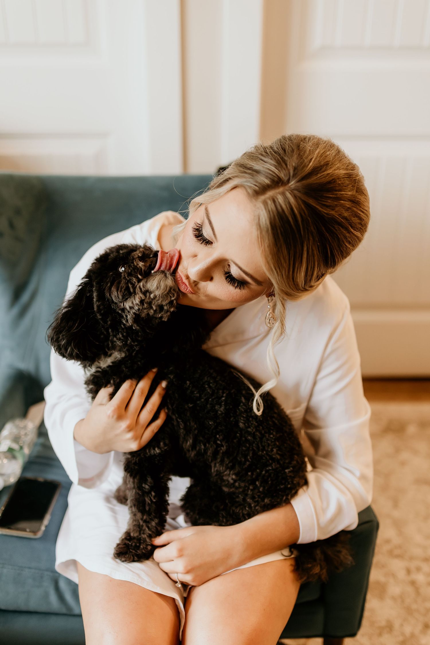 Person in white shirt cuddling with a black poodle or doodle dog on a carpeted floor.