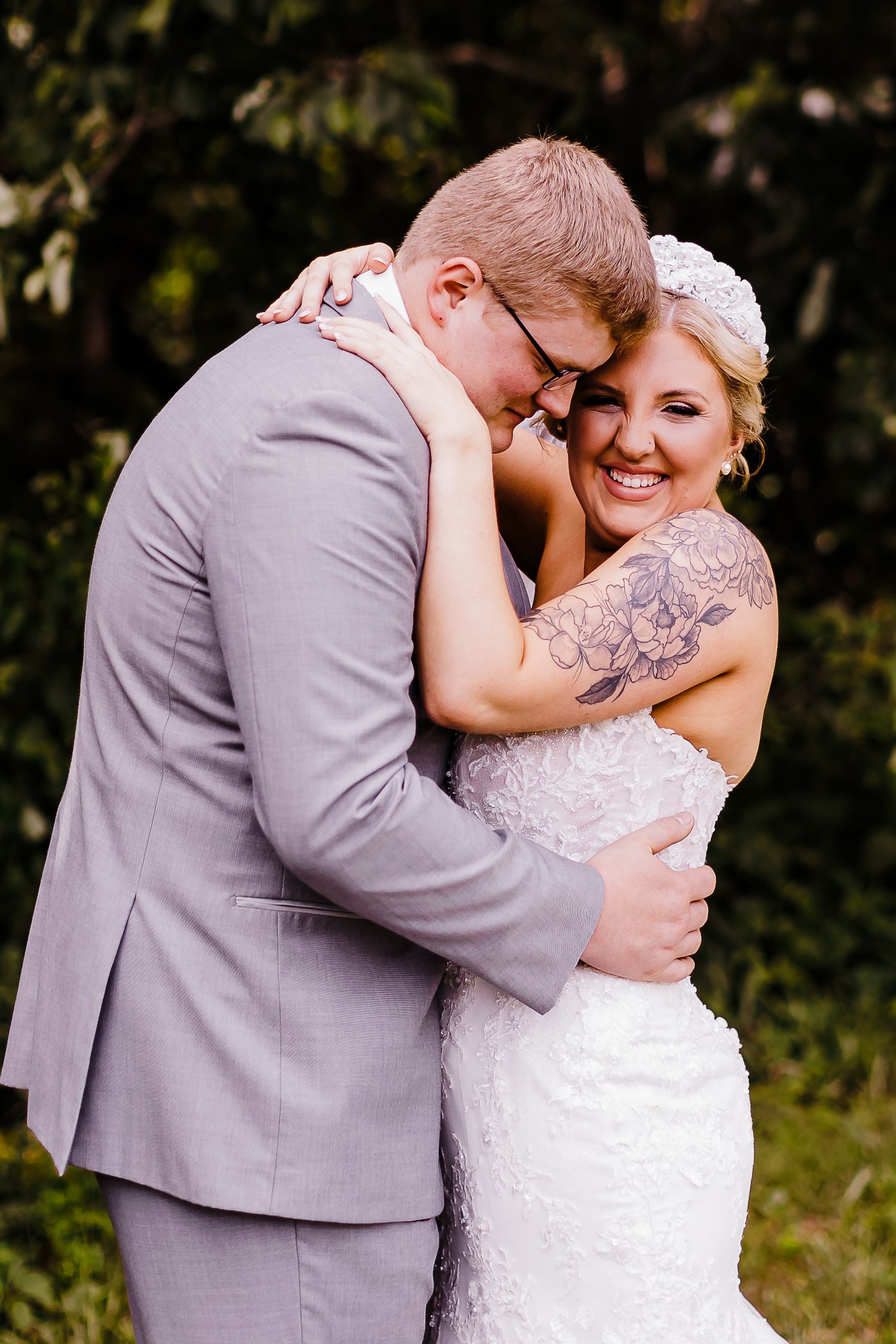 A tender moment between newlyweds as they embrace outdoors, with the bride in white lace and groom in gray.