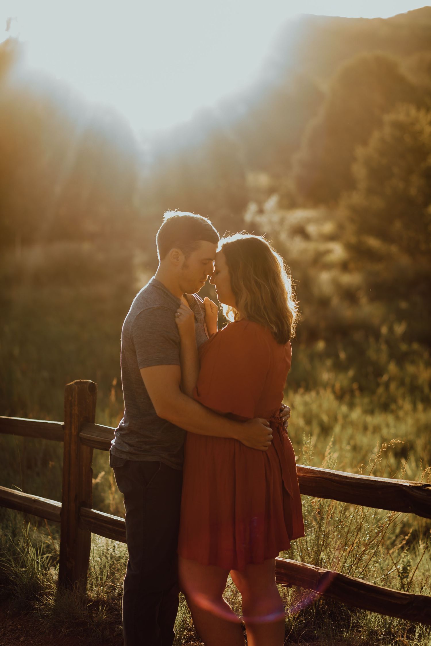 Couple embracing in golden sunset light near wooden fence.