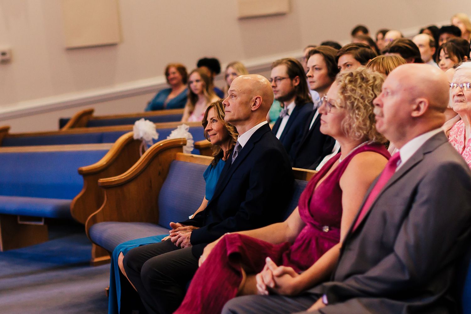 Wedding guests seated in church pews watching ceremony with attentive expressions.