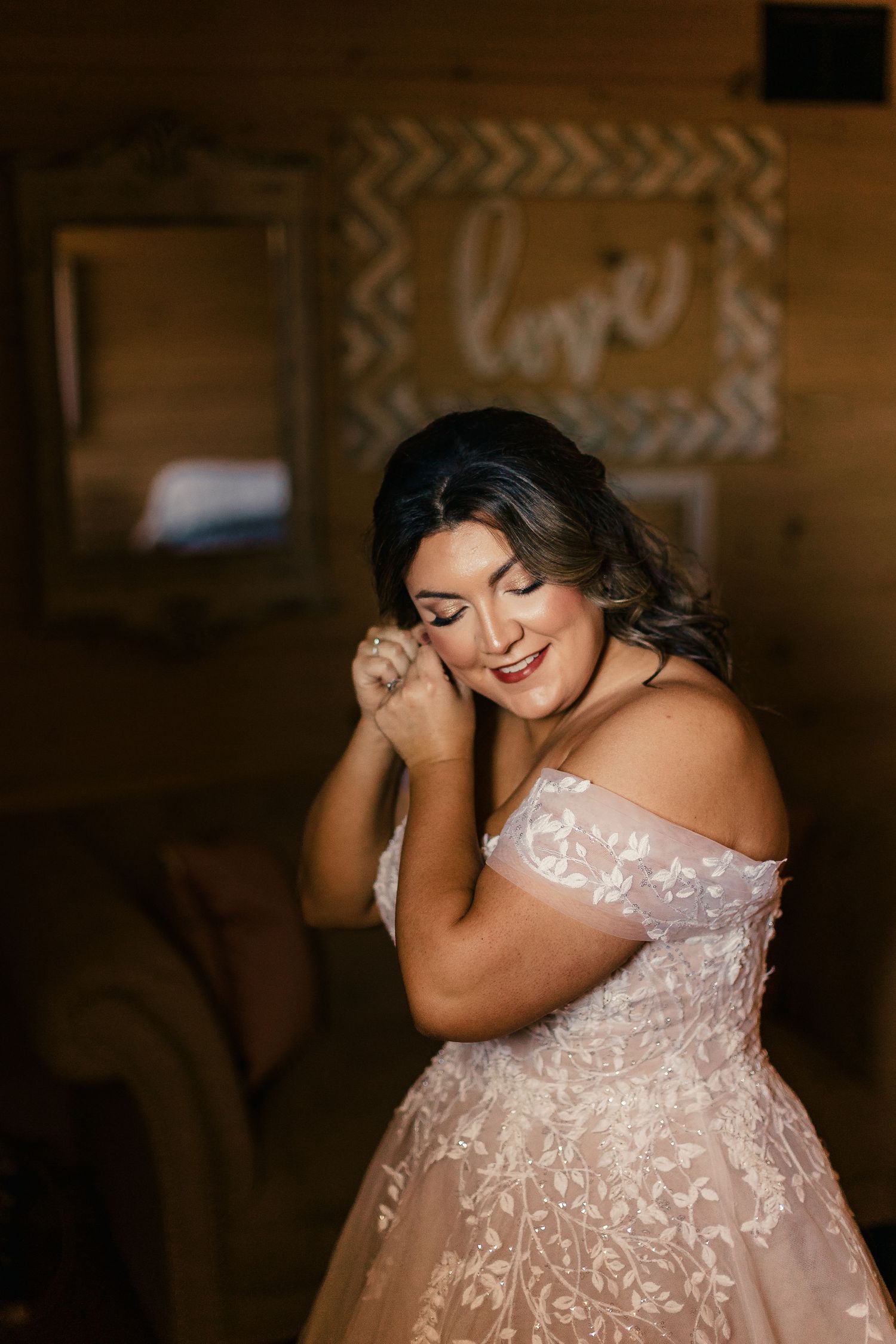 Close-up portrait of a bride wearing an elegant off-shoulder lace wedding gown in a rustic setting.