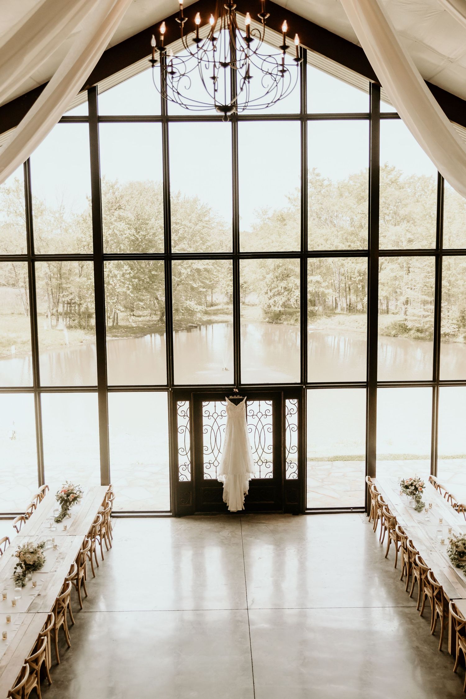 Spacious wedding venue with floor to ceiling windows overlooking a lake and white draped ceiling decor.