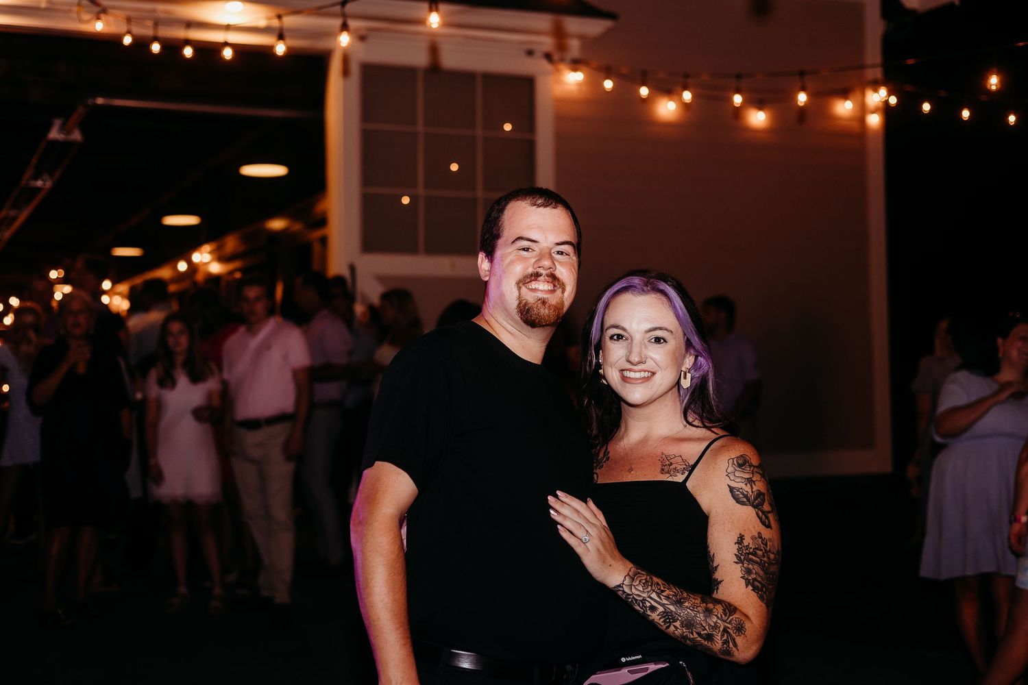 Couples dancing together during a dimly lit reception with string lights overhead and other guests in the background.