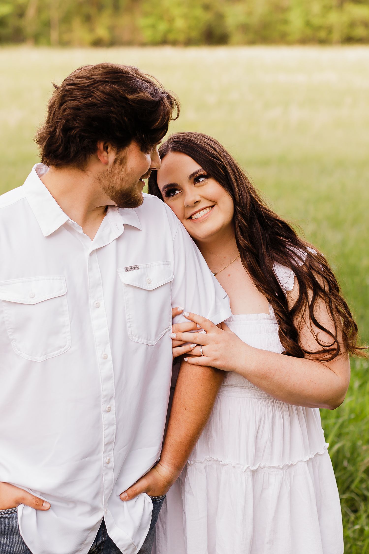A couple in white outfits shares a romantic moment in a sunny meadow.