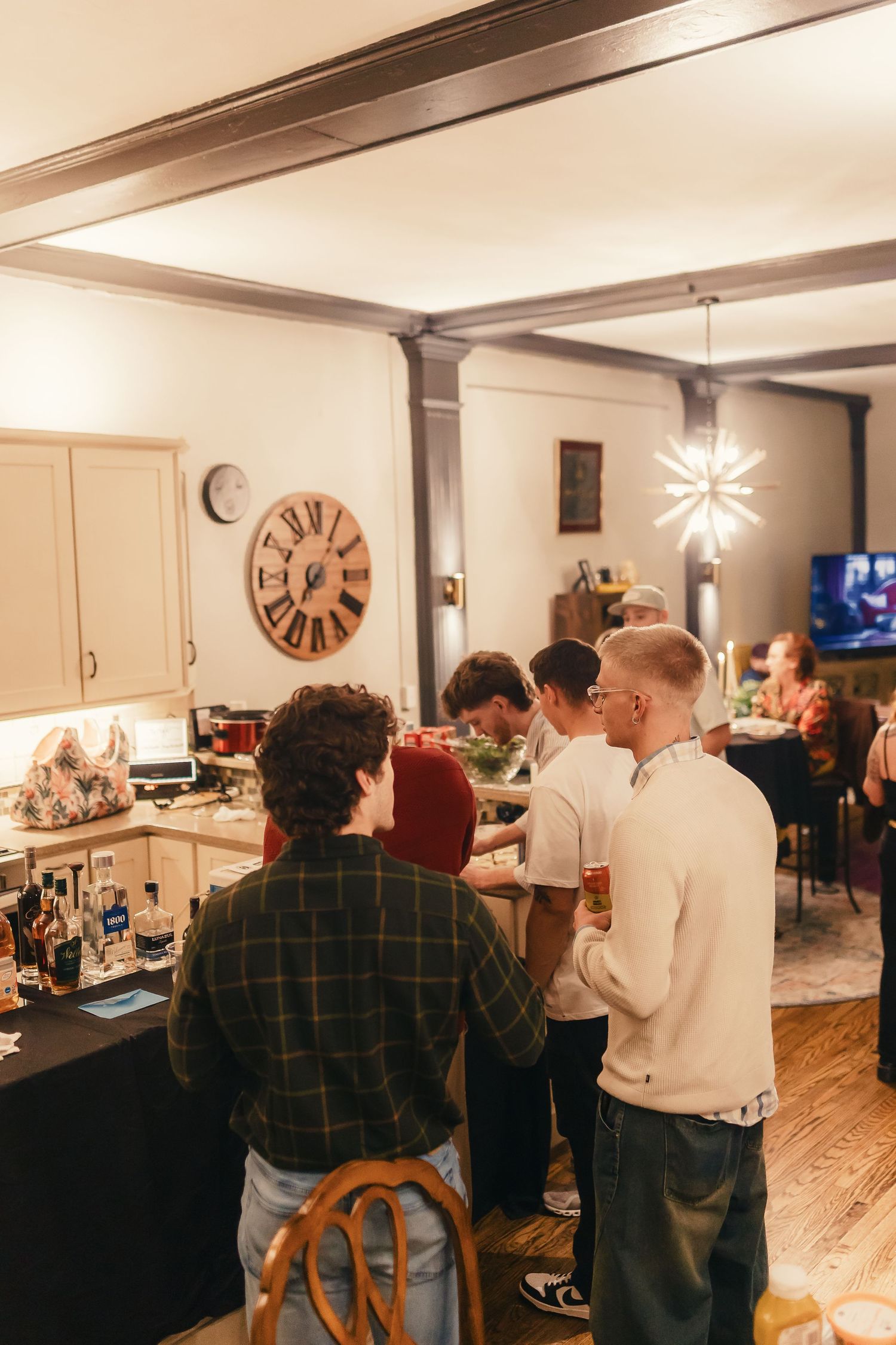 An indoor gathering with people mingling in a warmly lit room with white walls and decorative lighting.