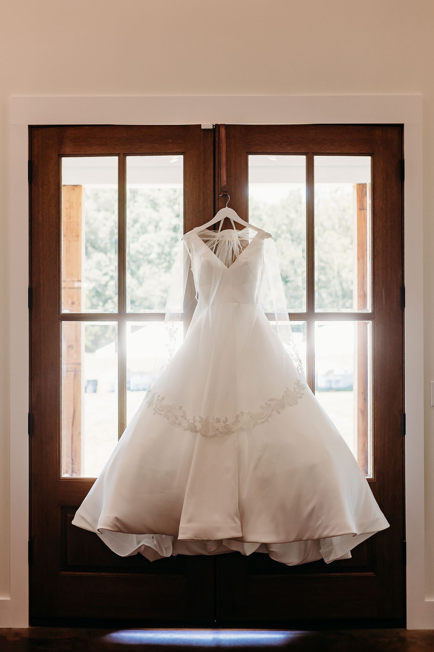 Elegant white wedding dress hanging in window light creating a beautiful silhouette.