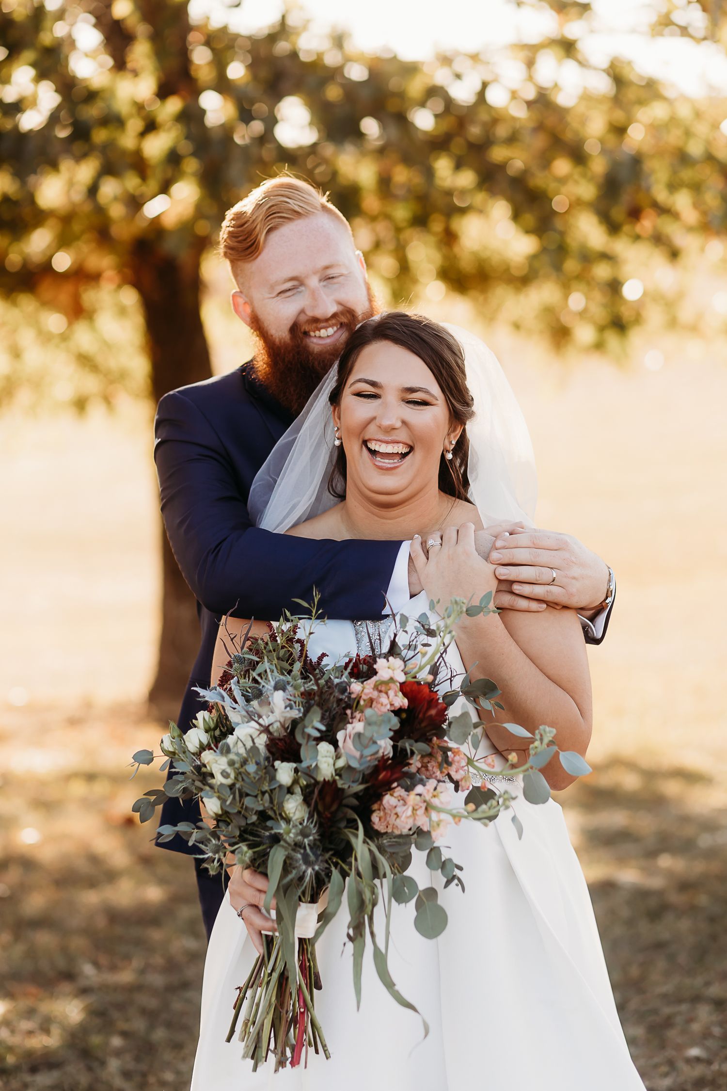 Joyful wedding portrait with bouquet of eucalyptus and roses in golden sunset light.
