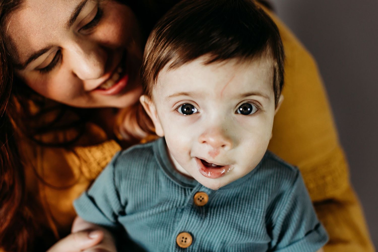 Close-up portraits of a baby wearing a teal outfit with wooden buttons.