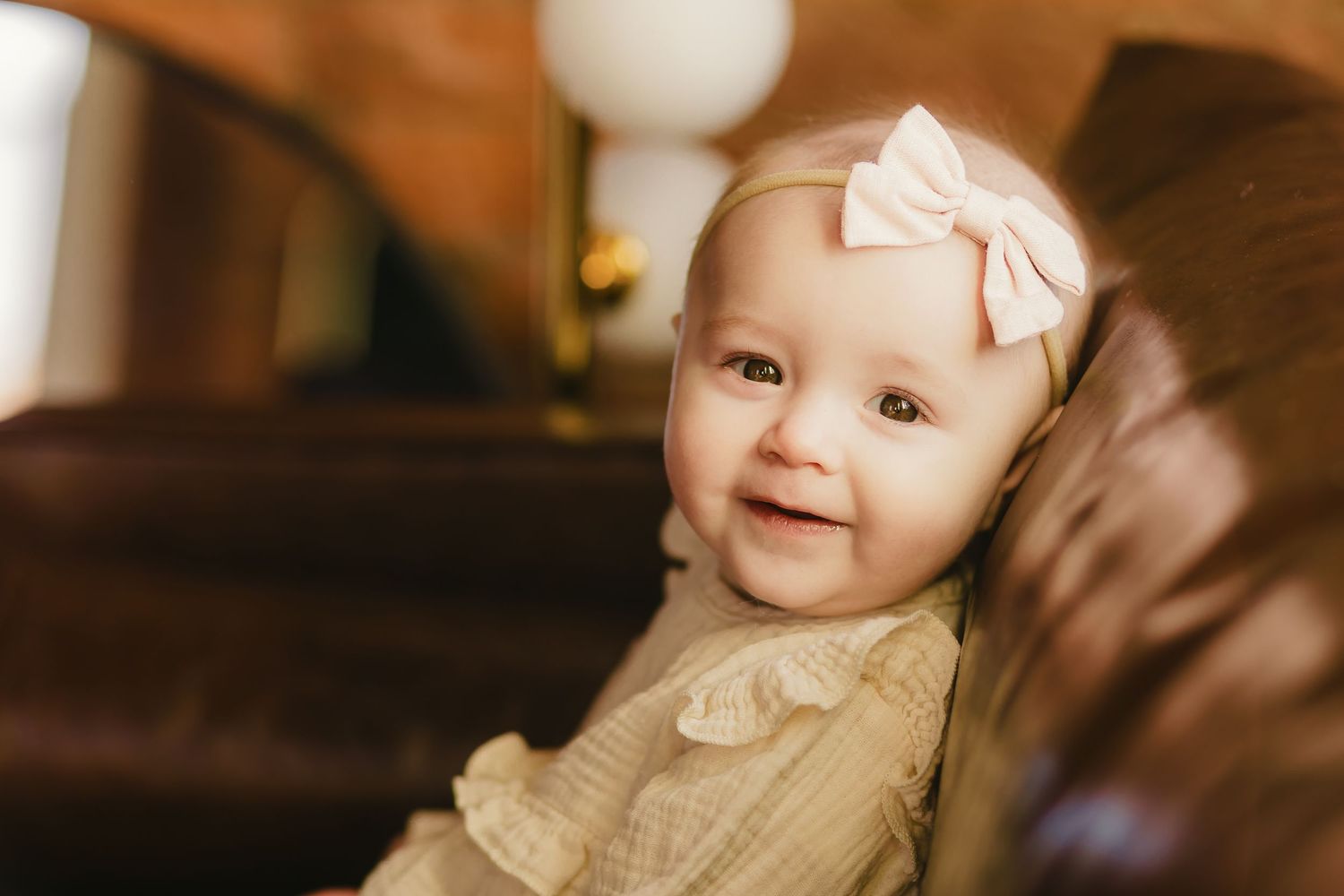 Baby in cream-colored outfit smiles while sitting indoors.