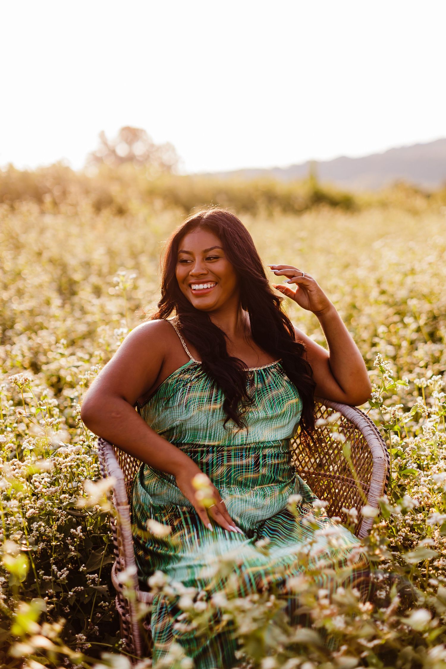 Person in green dress sitting among blooming wildflowers during golden hour.