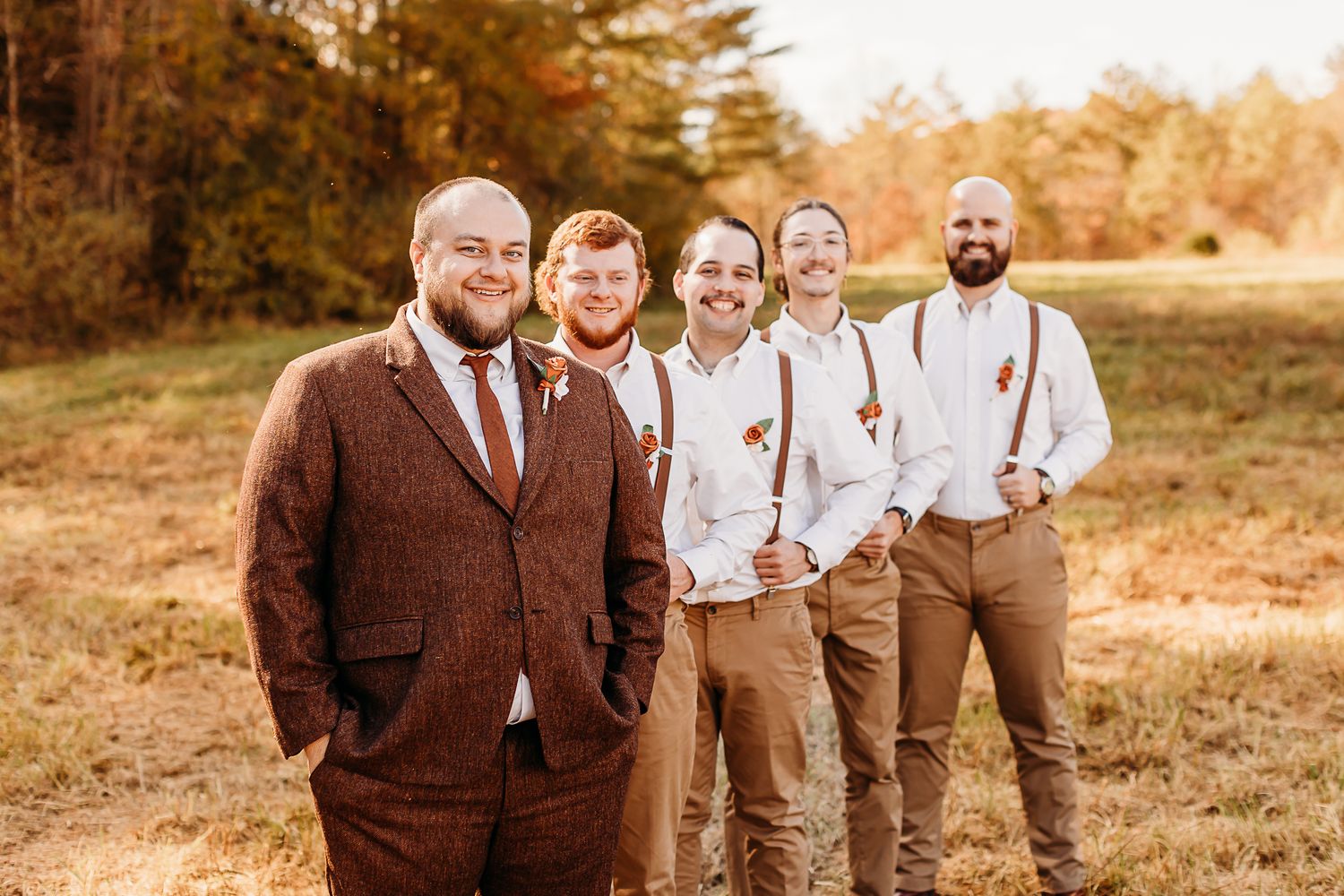 Groomsmen in brown suits and suspenders pose together outdoors during autumn.