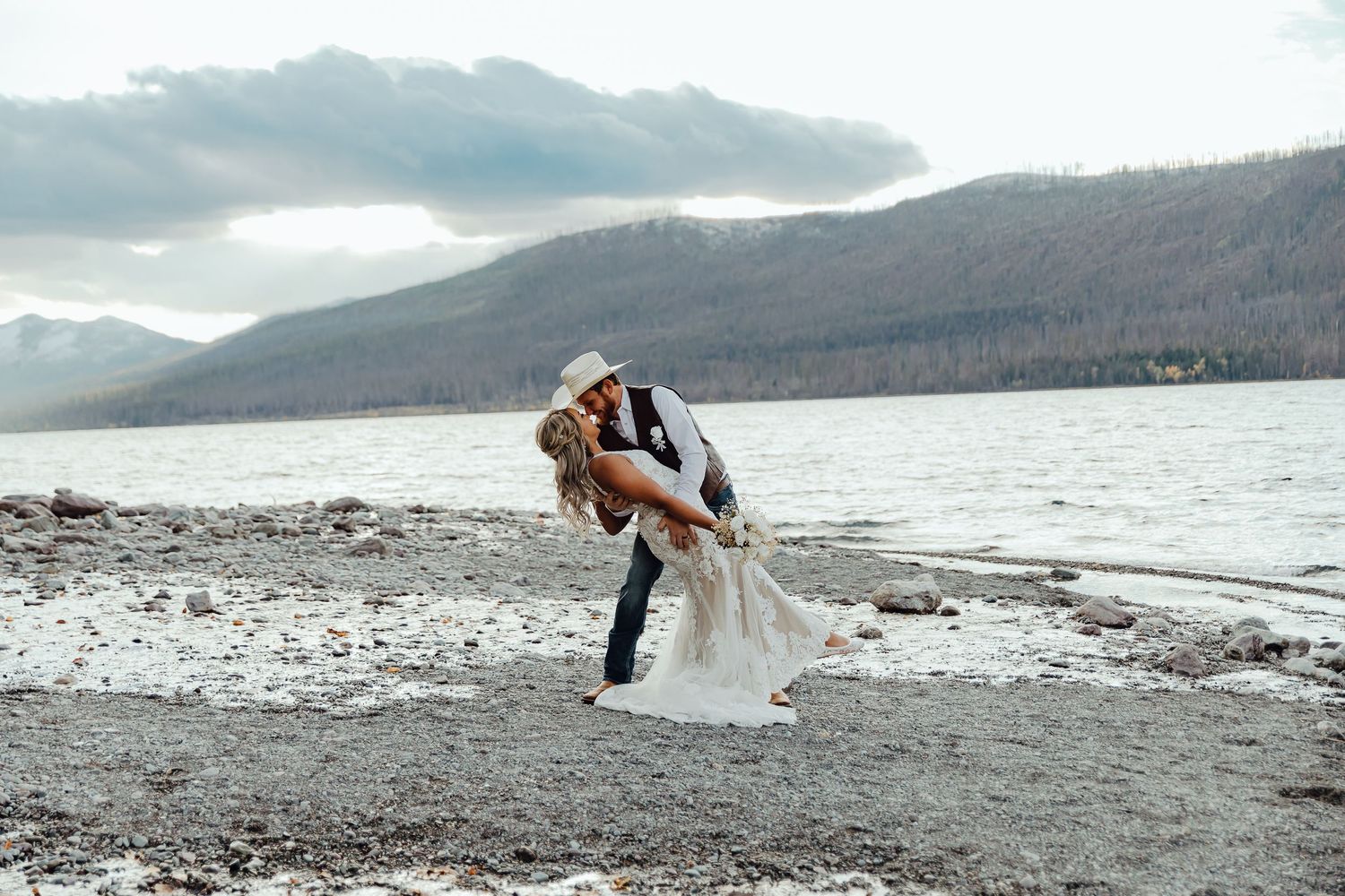 A romantic photoshoot on a rocky shoreline with dramatic mountain scenery in the distance.