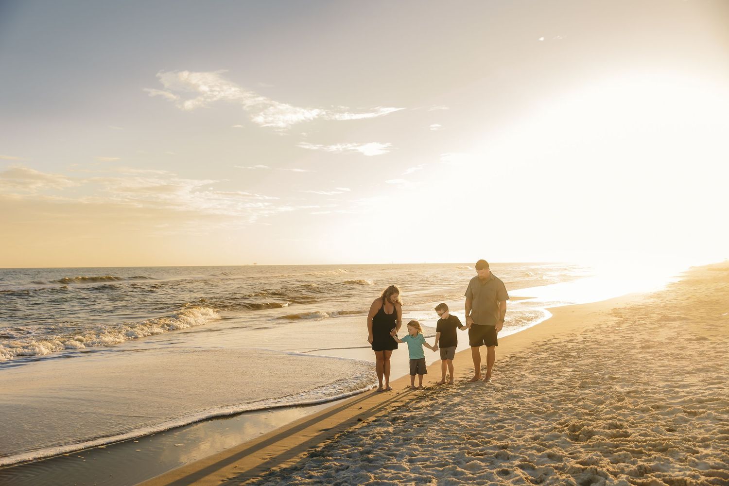 Family walks along beach shoreline during sunset with beautiful golden light.