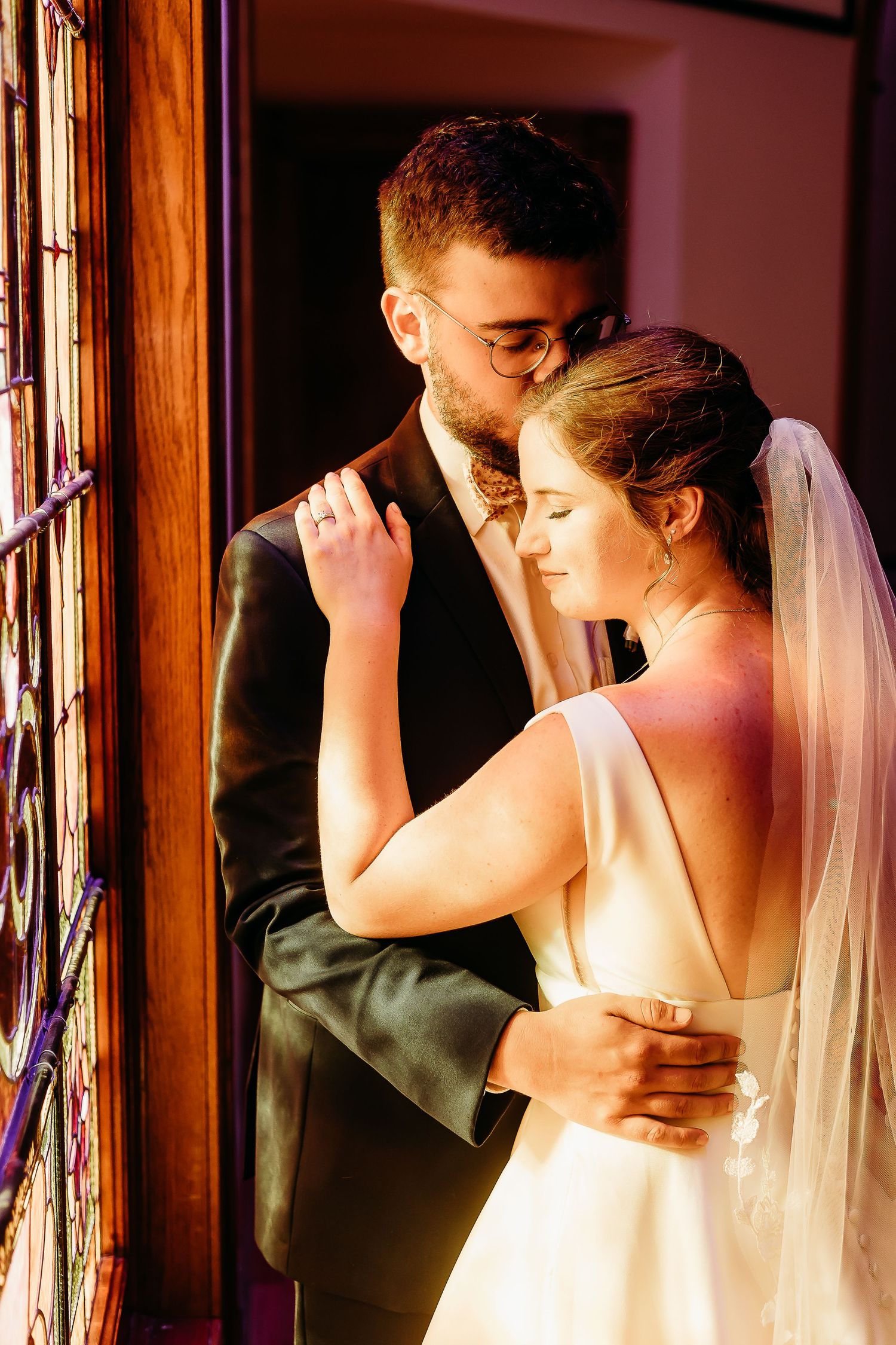 Intimate wedding moment captured near stained glass windows in warm lighting.