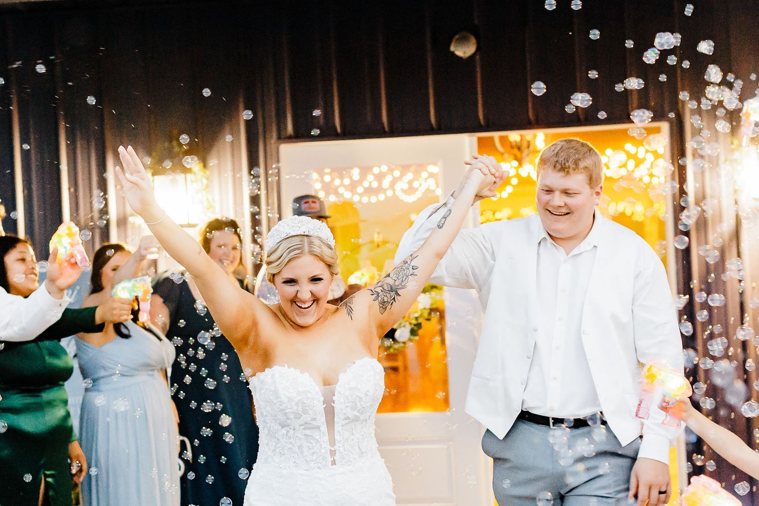 Wedding reception celebration with guests dancing under twinkling lights and bubbles.