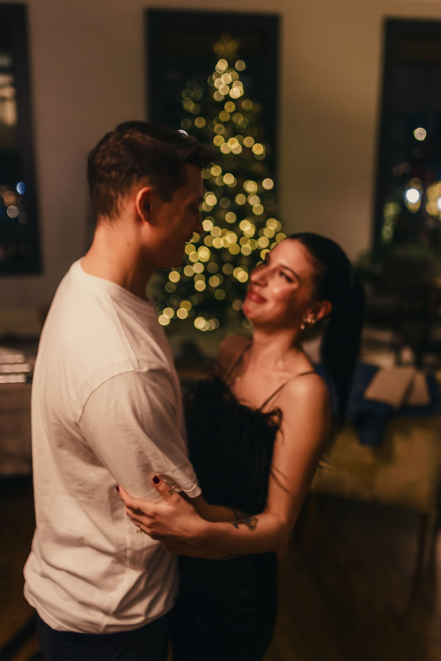 A couple dances intimately in a dimly lit room with a Christmas tree glowing in the background.