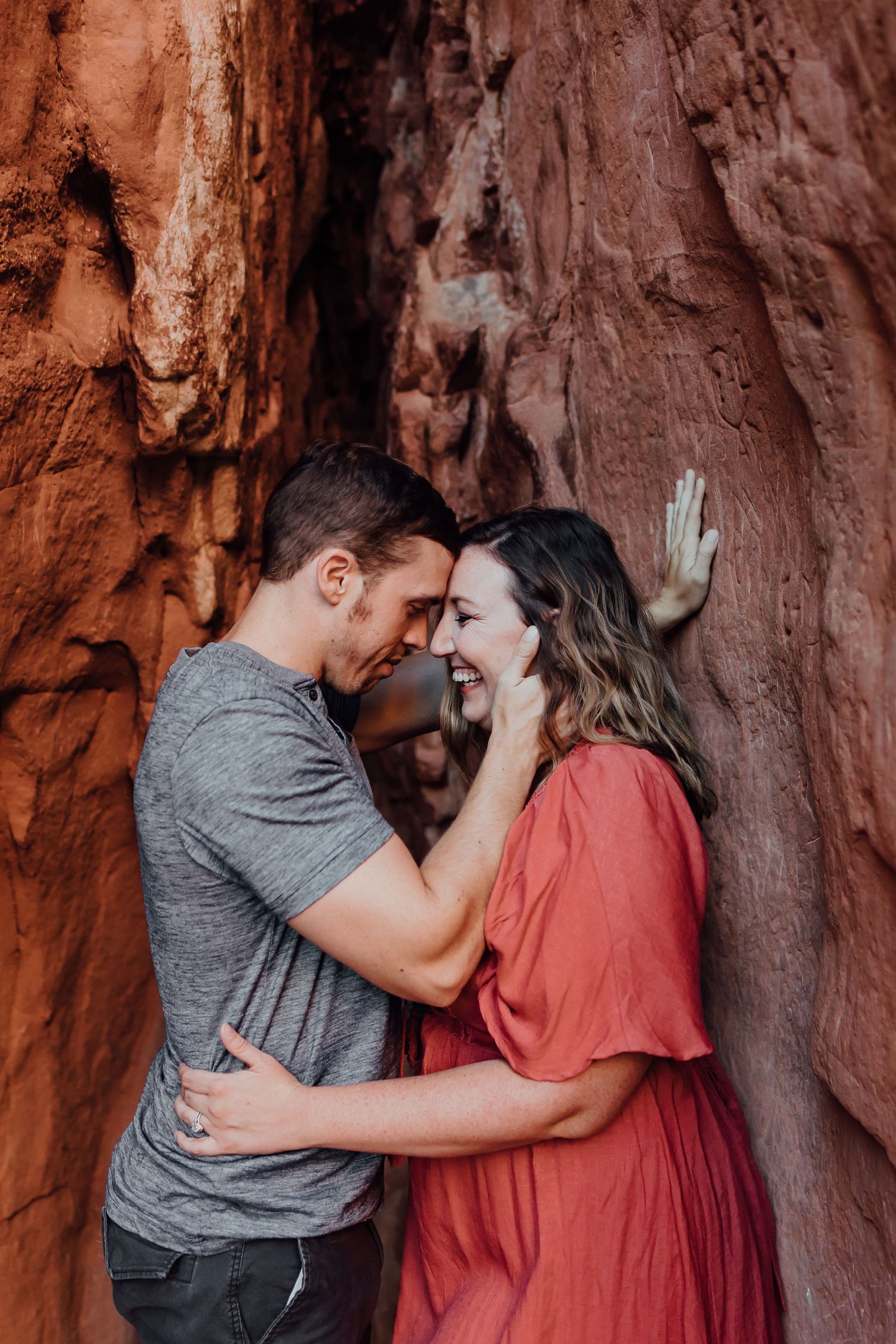Intimate portrait against red rock wall showing tender embrace.