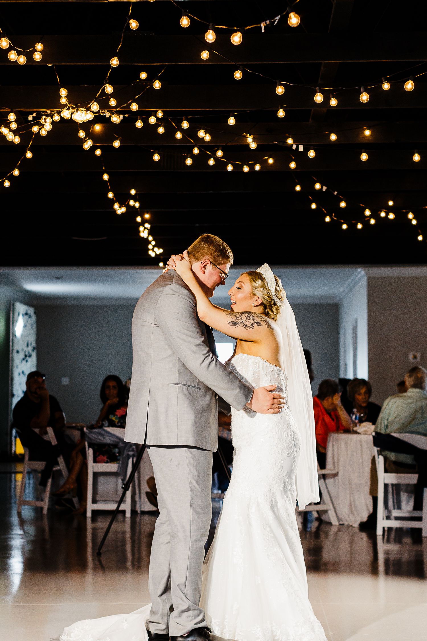 Newlyweds share their first dance under warm string lights in an elegant reception venue.