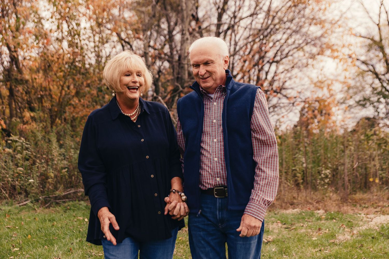 An elderly couple shares a joyful moment together outdoors during autumn.