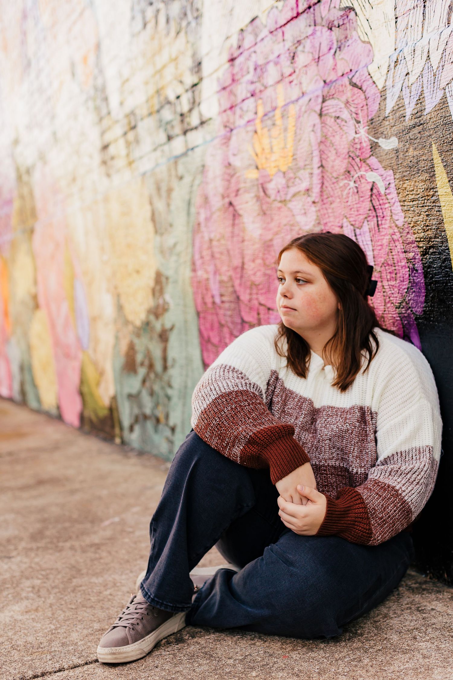 Person sitting against colorful wall wearing knit sweater and dark pants.