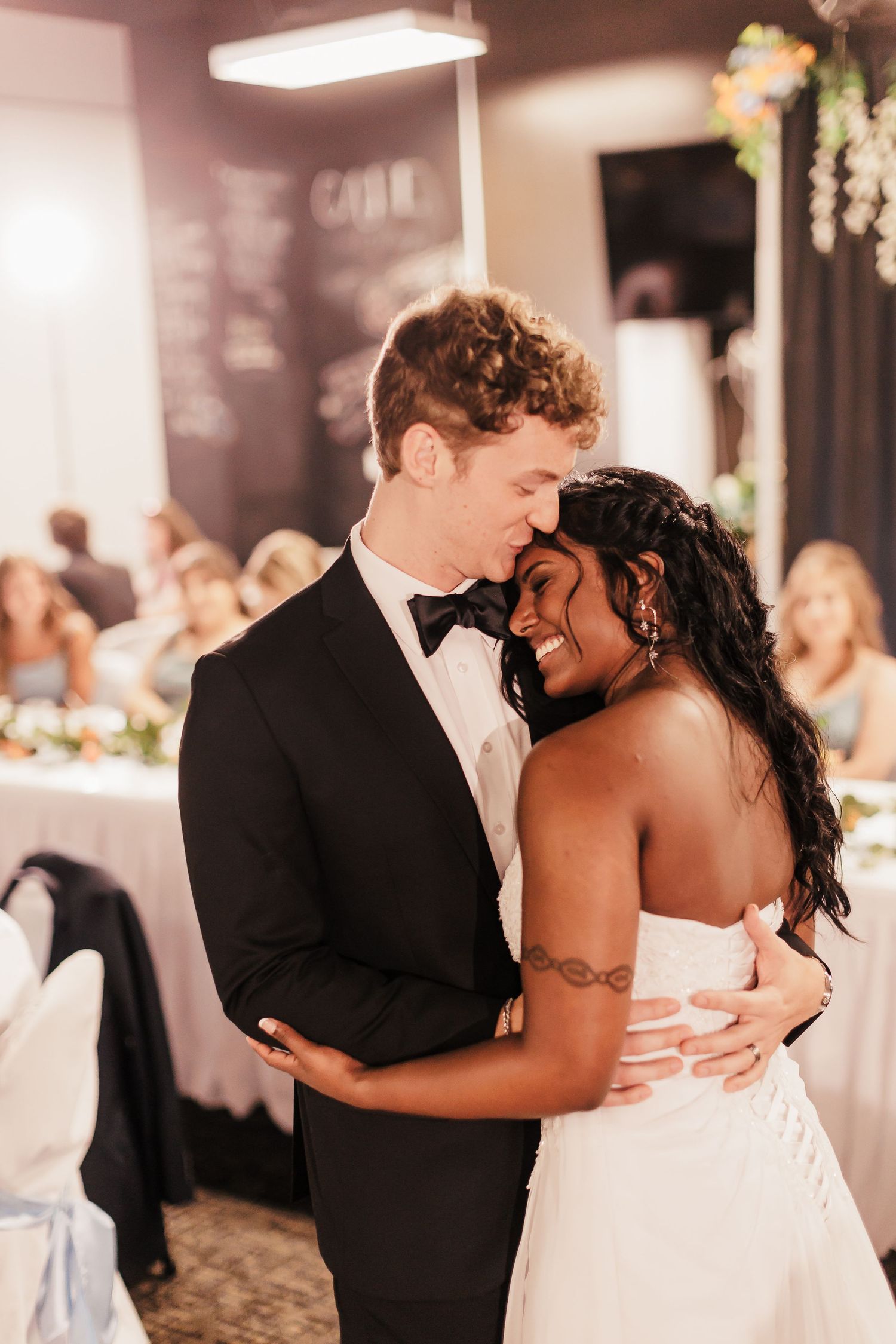 Couple shares intimate dance moments at dimly lit indoor reception.