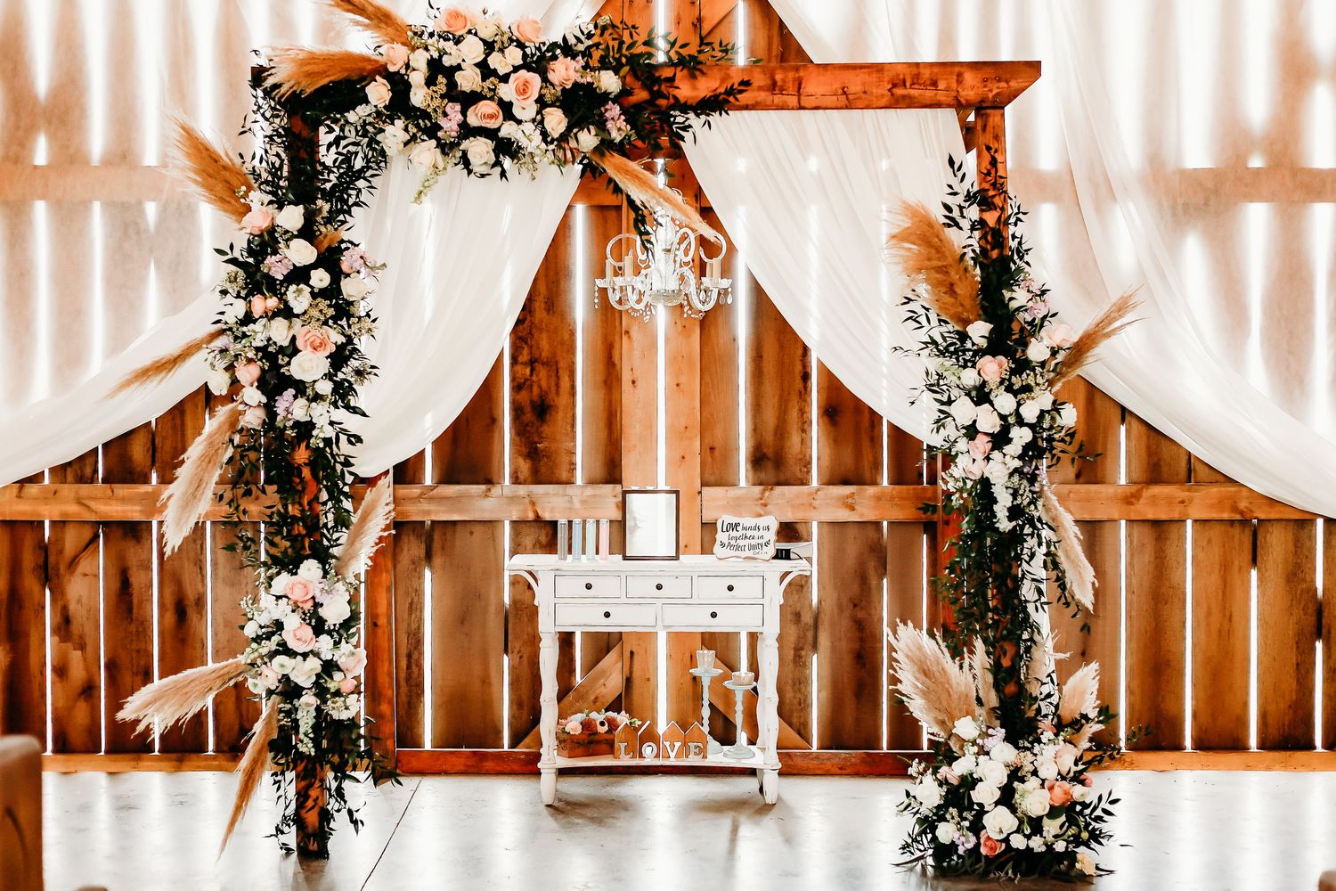 Wedding ceremony space decorated with white floral arrangements and draped fabric.