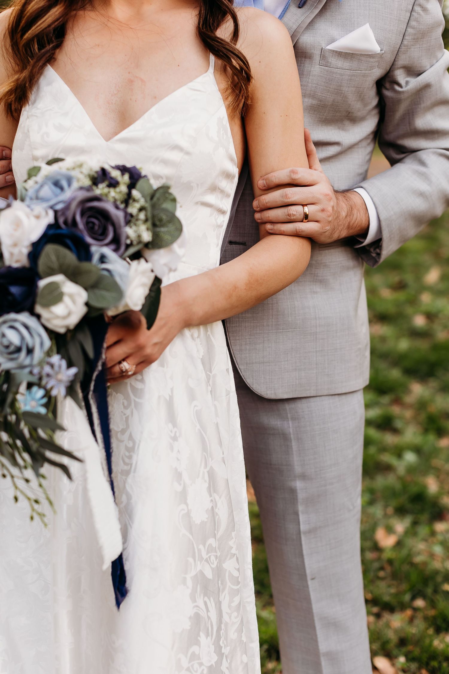 Wedding couple holding blue and white floral bouquet with grey suit and white dress details.