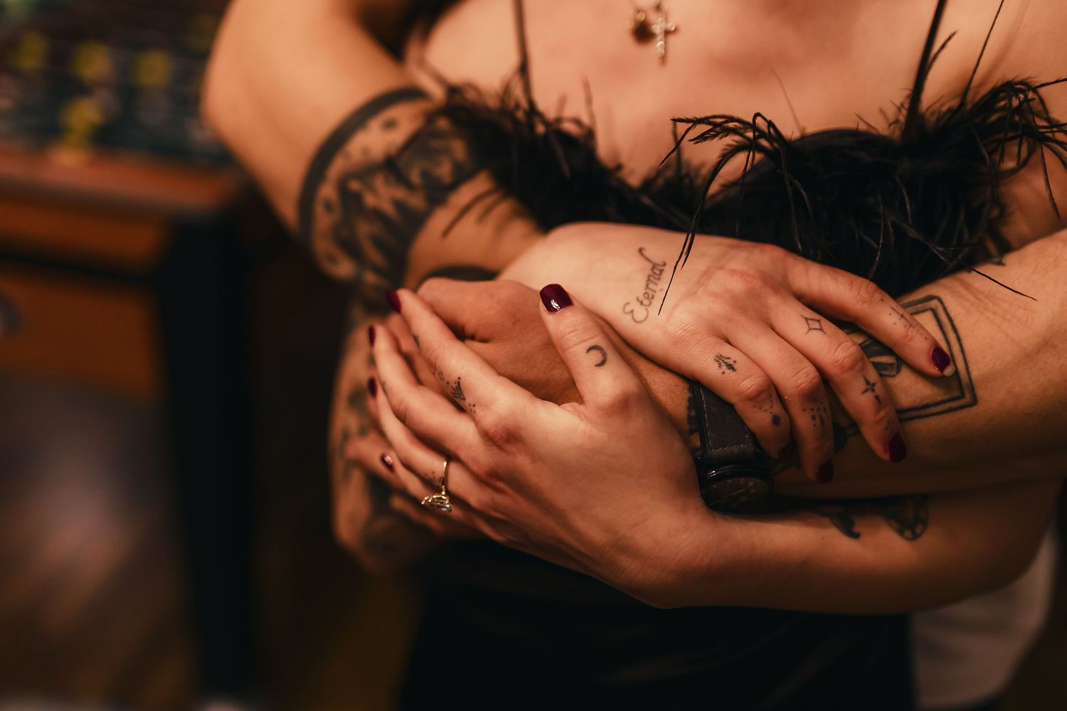 Close-up of hands with black lace sleeves and delicate jewelry embracing in an intimate pose.
