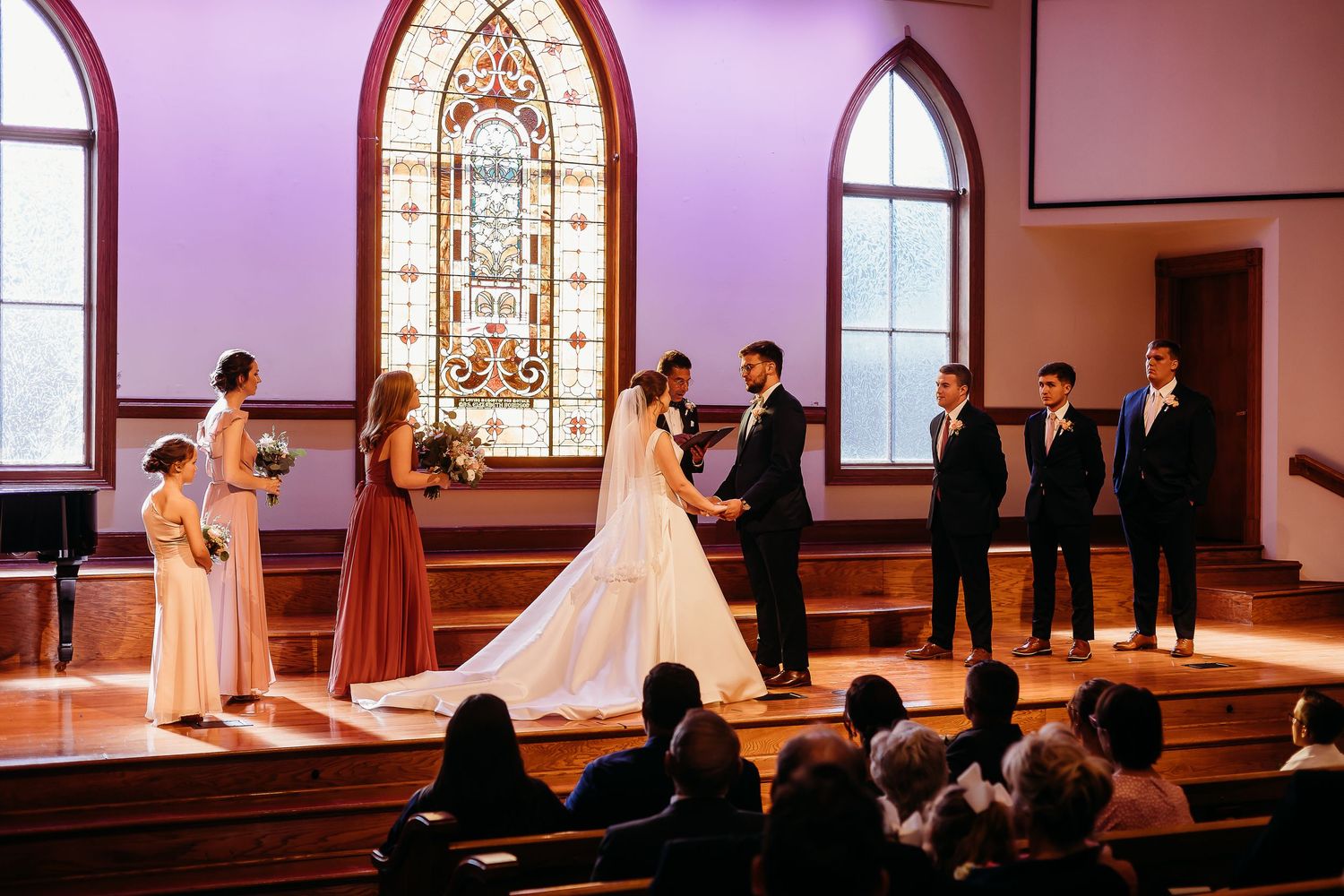 Wide shot of wedding ceremony in a church with stained glass windows and purple lighting.