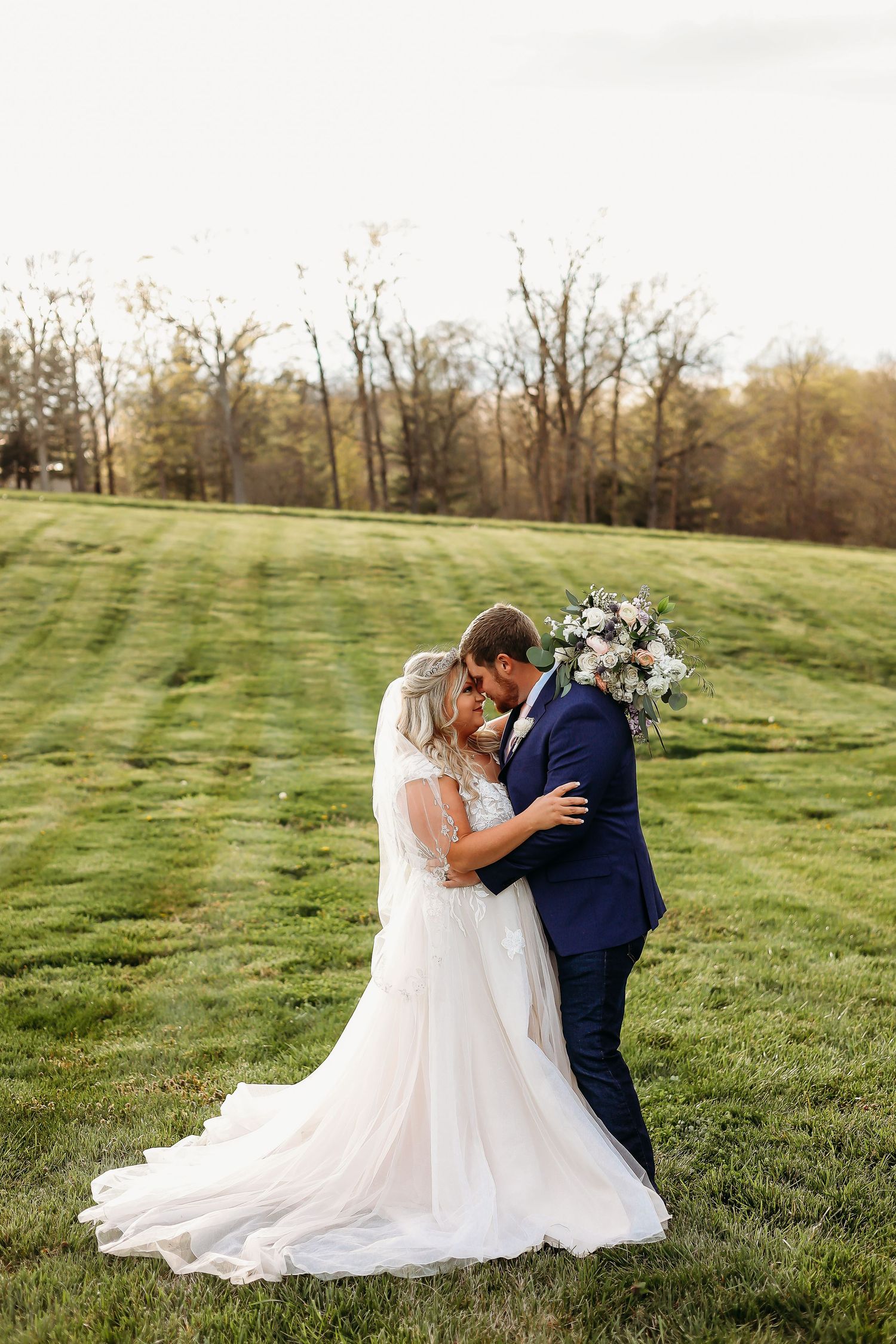 Romantic wedding couple sharing an intimate moment on a grassy hillside during golden hour.