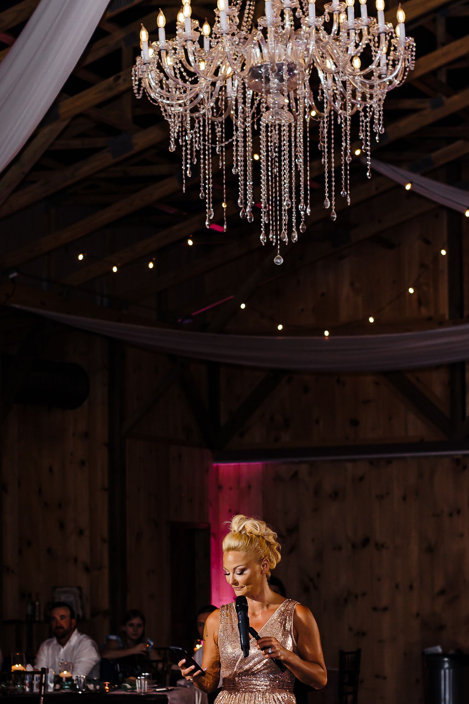 Elegant crystal chandelier illuminates rustic barn venue during evening celebration.