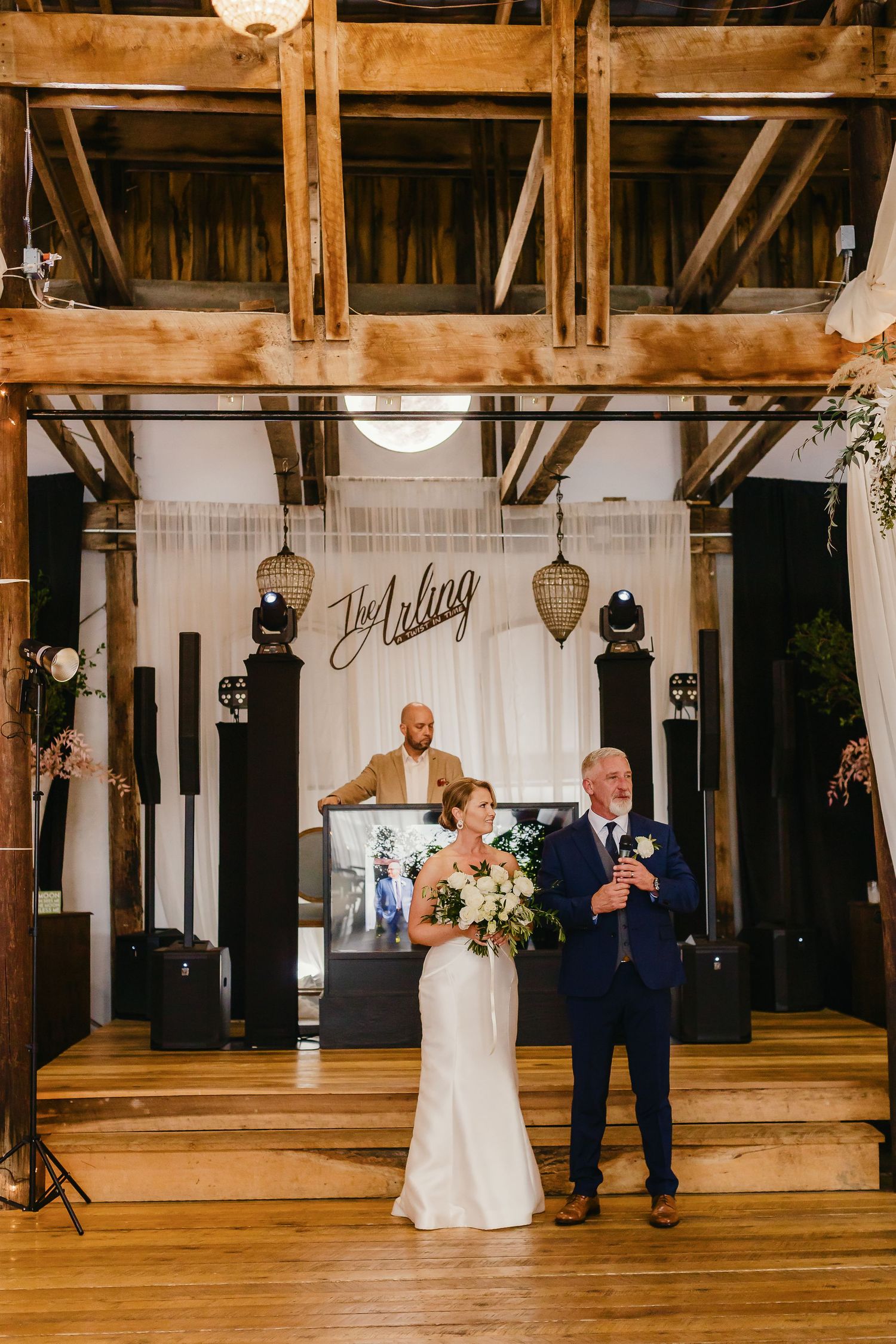 Wedding couple dances together in a rustic wooden barn venue with exposed beams and white draping decorations.