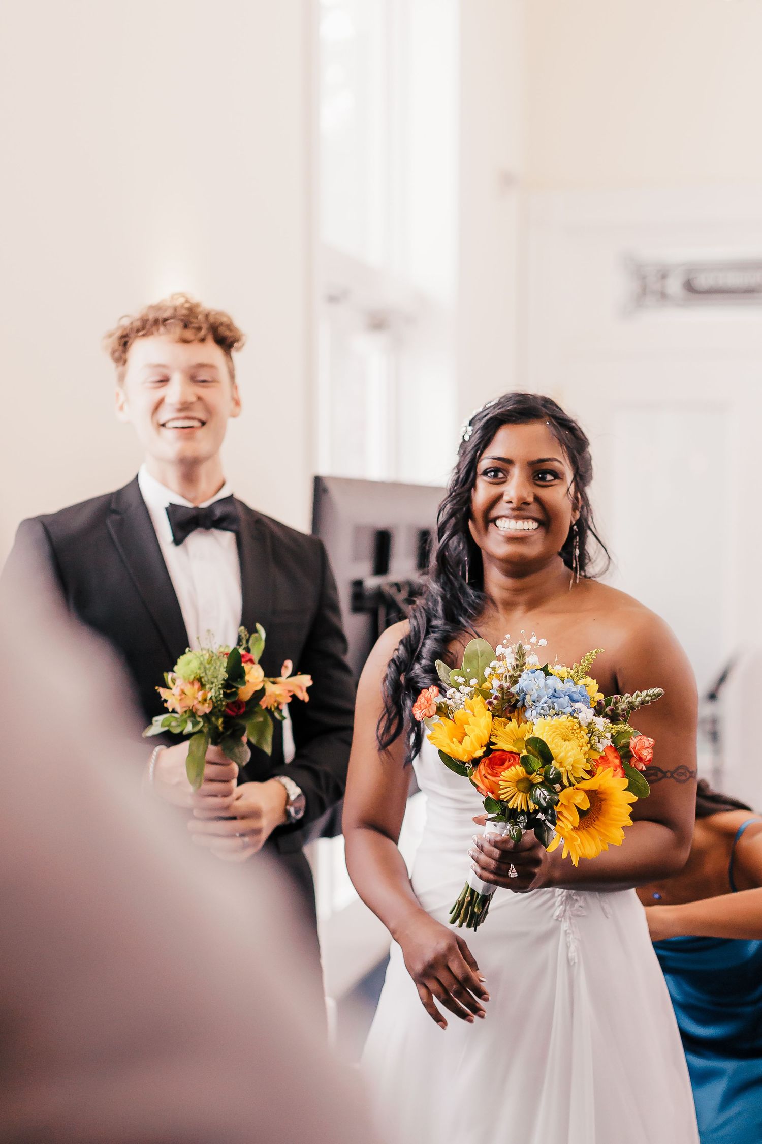 Wedding couple sharing joyful moment while holding vibrant sunflower bouquets.