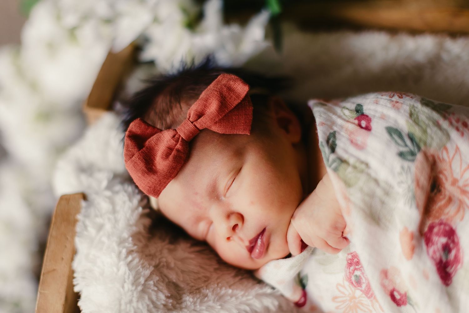 Sleeping newborn wearing a coral bow headband and floral outfit.