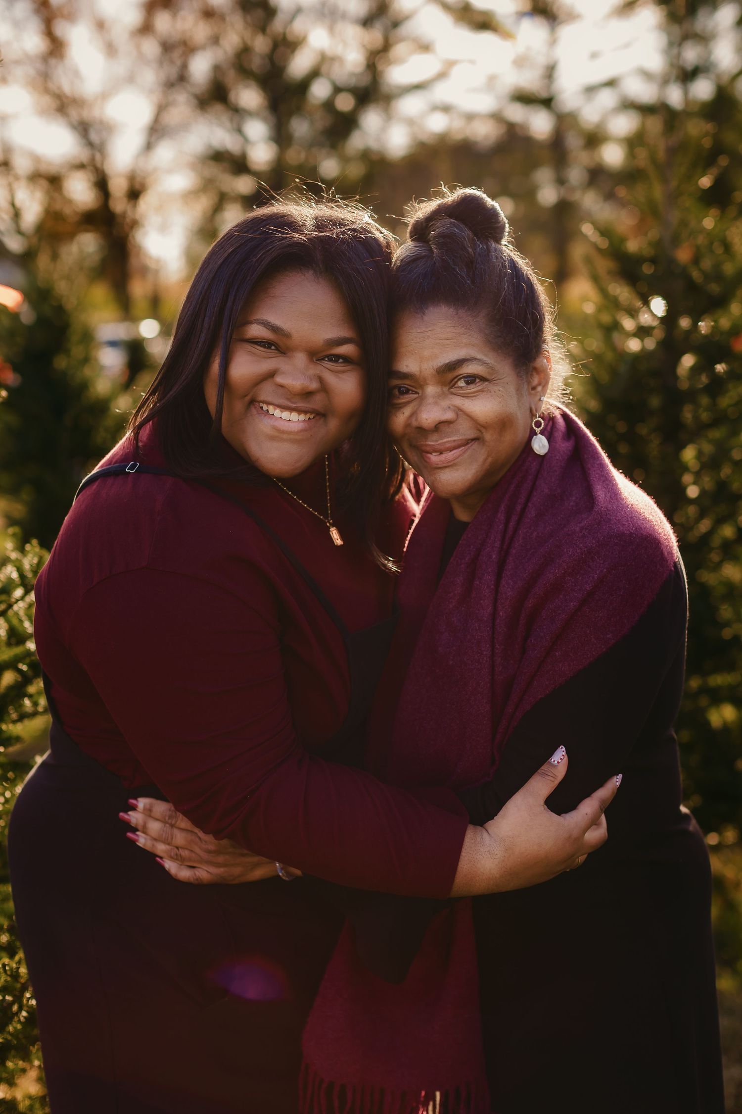 Two women in burgundy sweaters sharing a warm embrace outdoors at sunset.