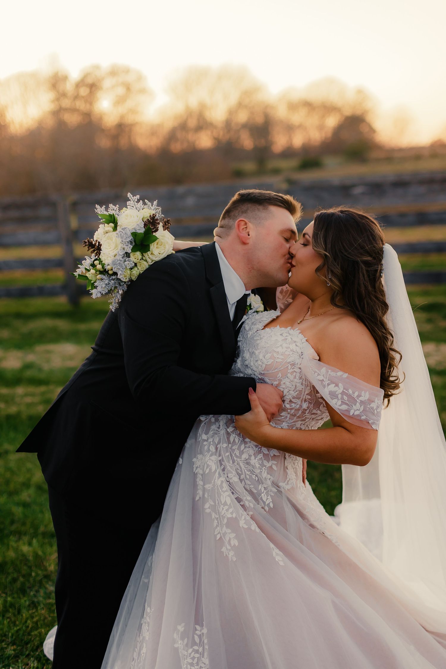 Romantic sunset portrait of newlyweds kissing in an outdoor field setting.