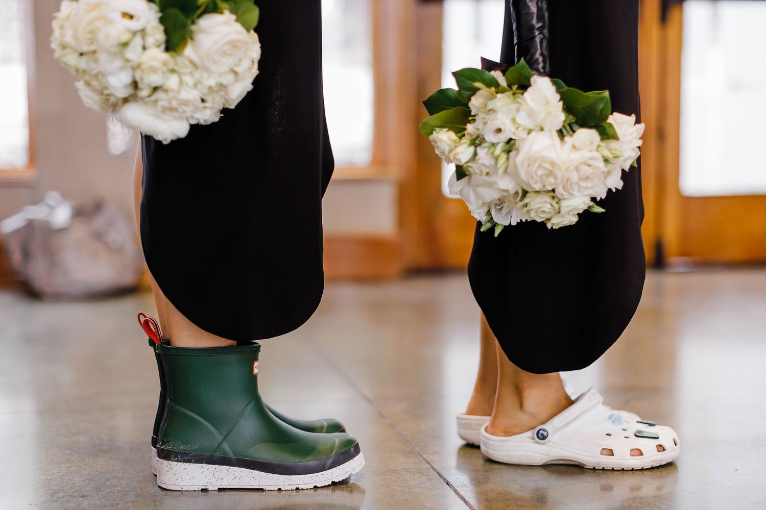 Detail shot of wedding attire showing green rain boots and formal shoes on wooden floor.