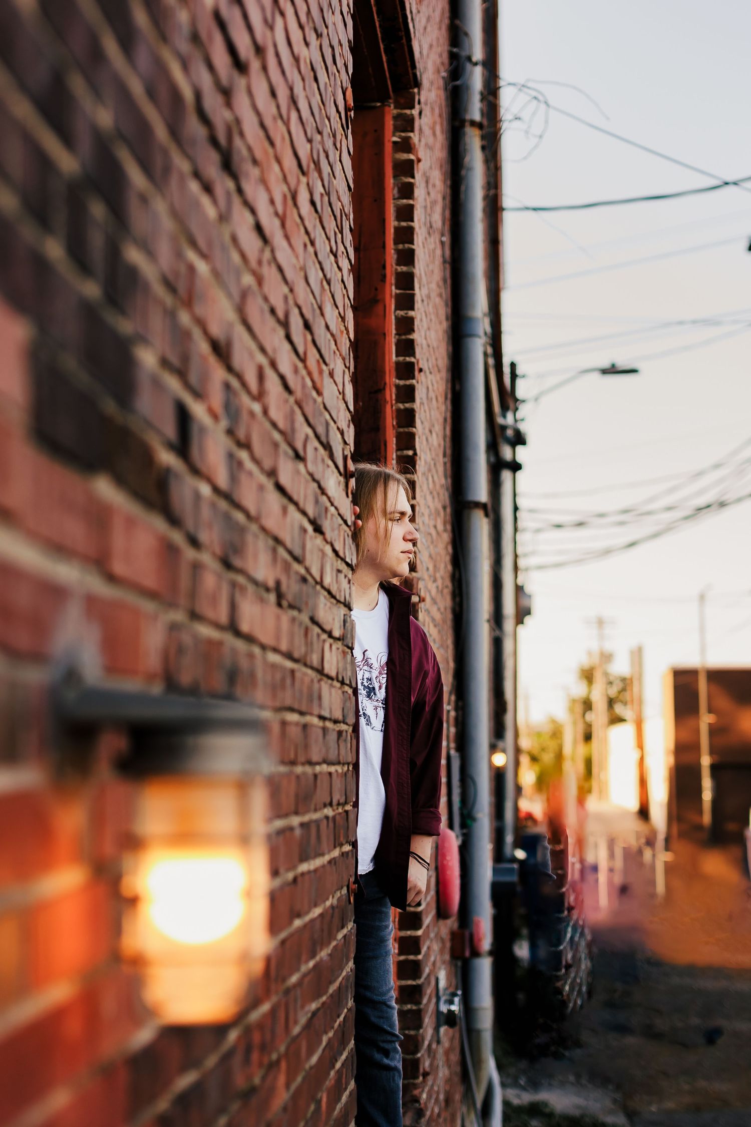 Person leaning against brick wall at sunset with warm lighting.