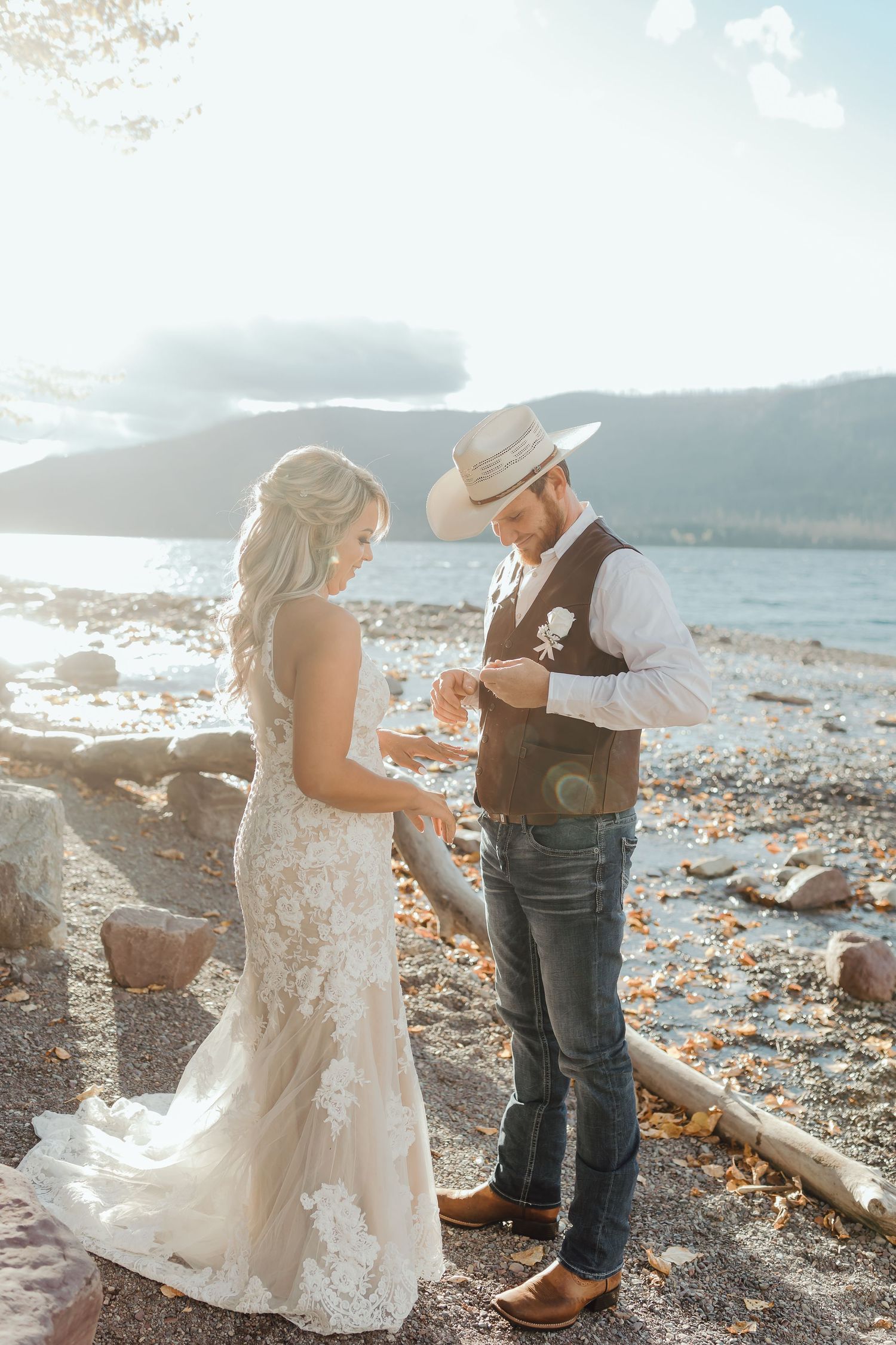 A romantic wedding moment captured on a rocky beach with mountains and water in the background.