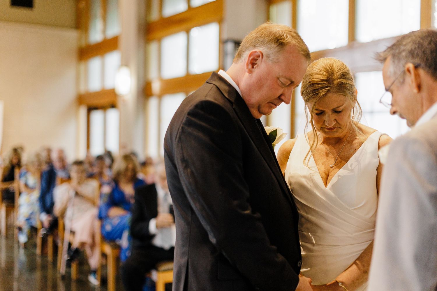 Indoor wedding ceremony in a sunlit venue with guests watching the proceedings.