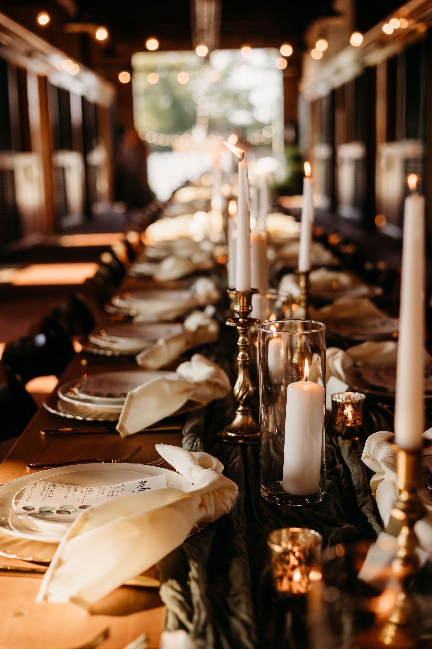 Elegant wedding reception table setting with white candles and place settings in warm lighting.