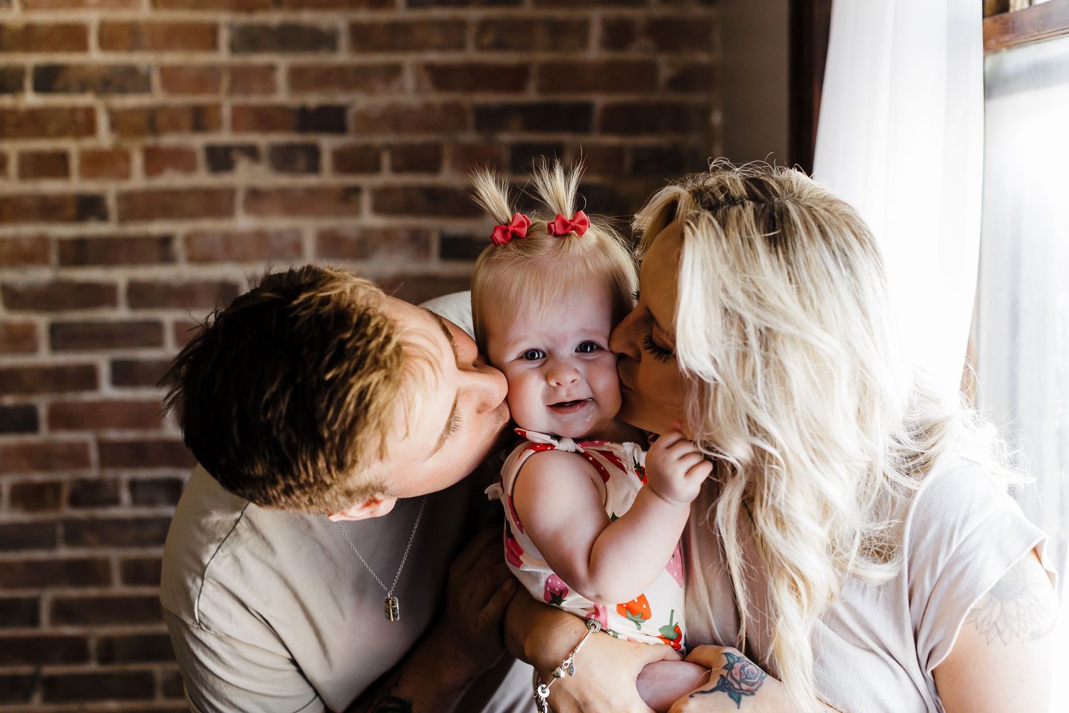 A family shares a tender moment with their baby against a brick wall background.