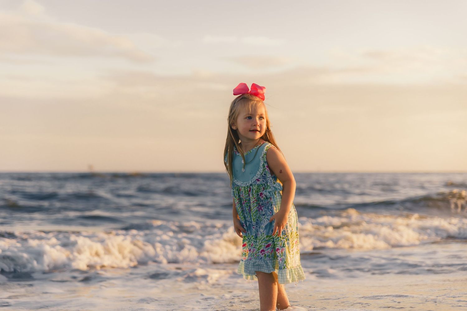 Family playing and splashing in ocean waves at sunset on a sandy beach.