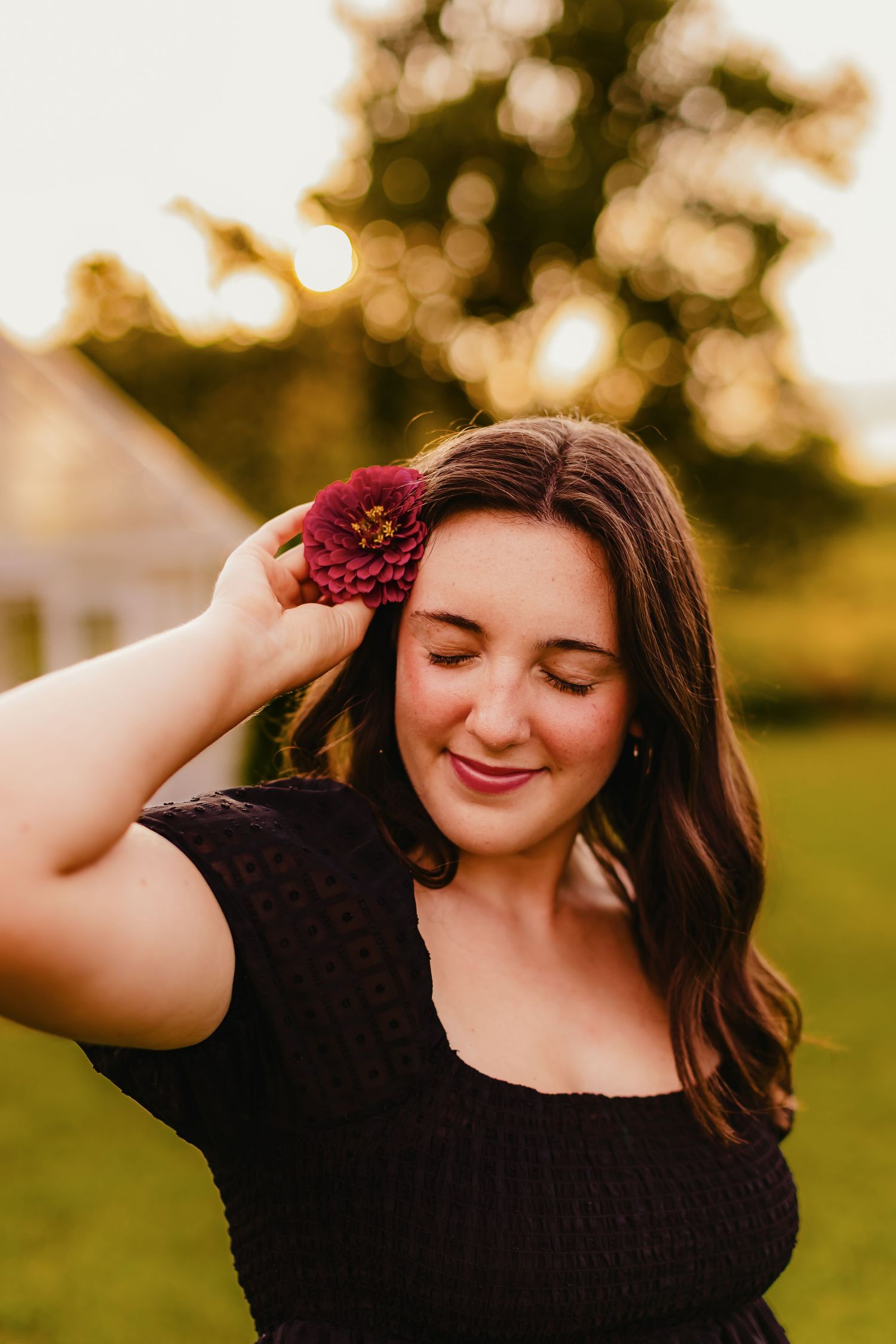 A person in a black lace dress poses outdoors during golden hour with soft bokeh lighting effects.