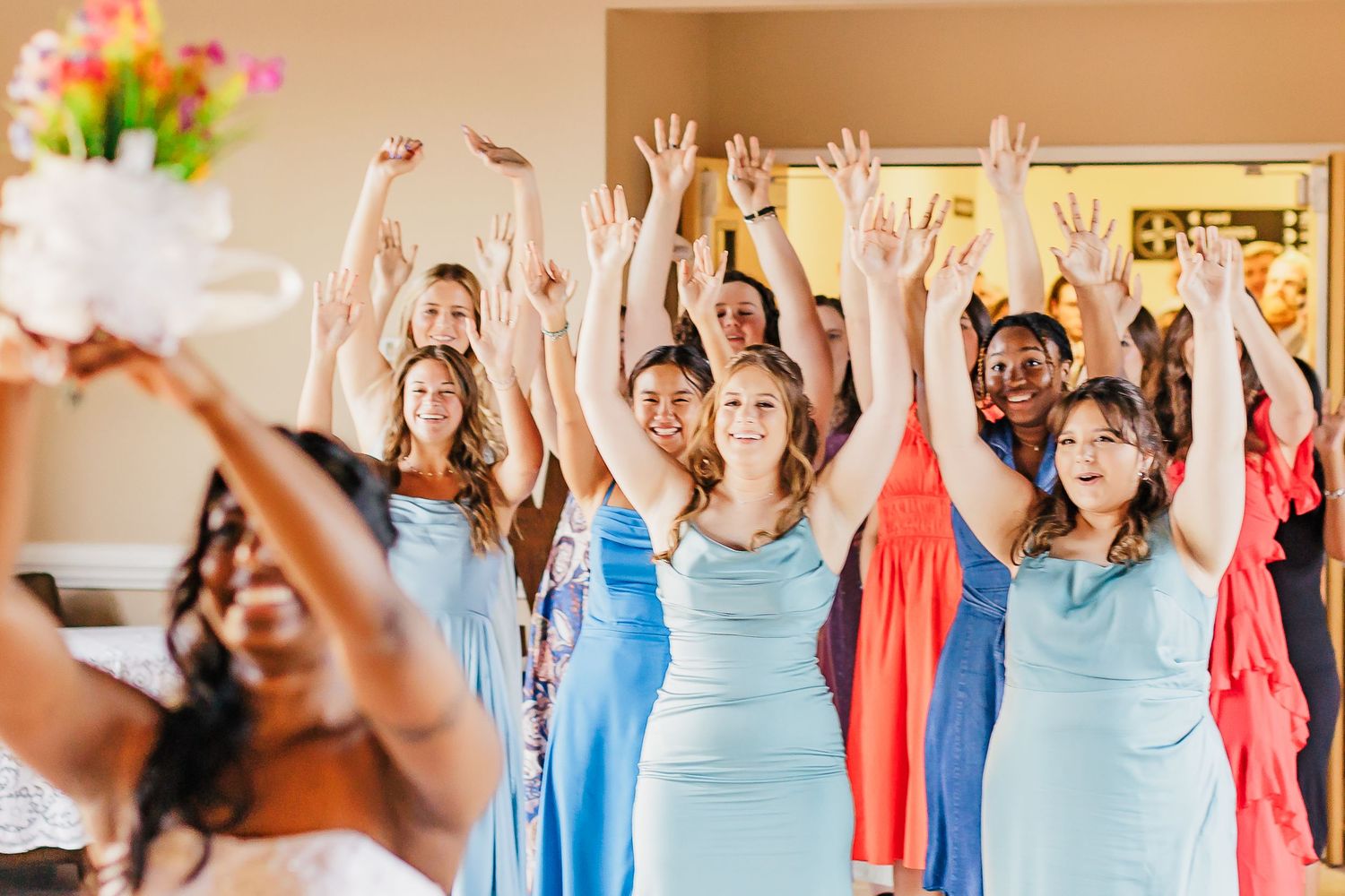Wedding party celebrates joyfully in light blue bridesmaid dresses and coral accents at an indoor venue.